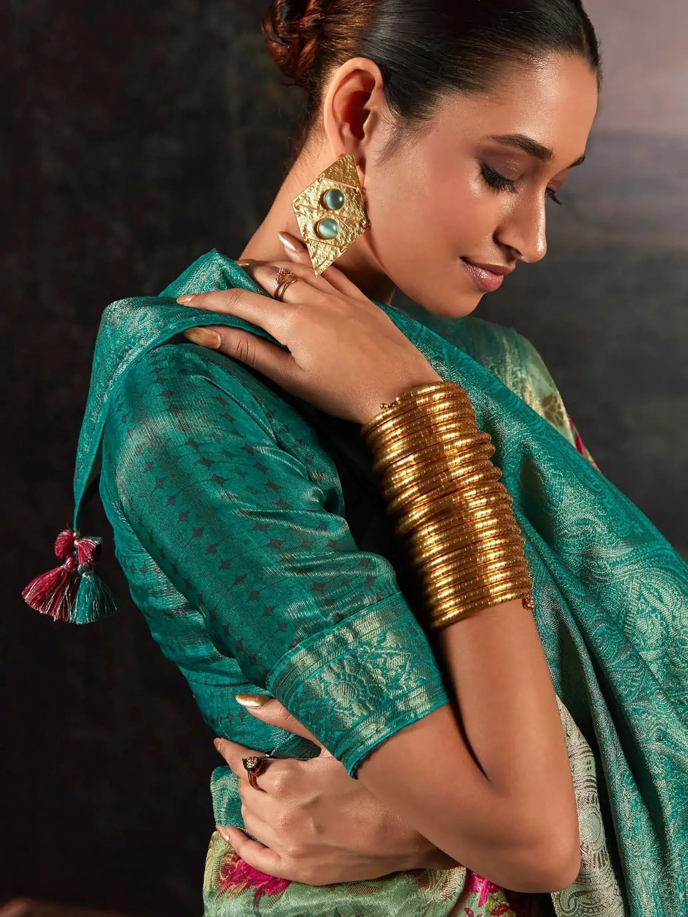 Woman in emerald green ethnic saree with gold jewelry and tassels, perfect for Indian occasions.