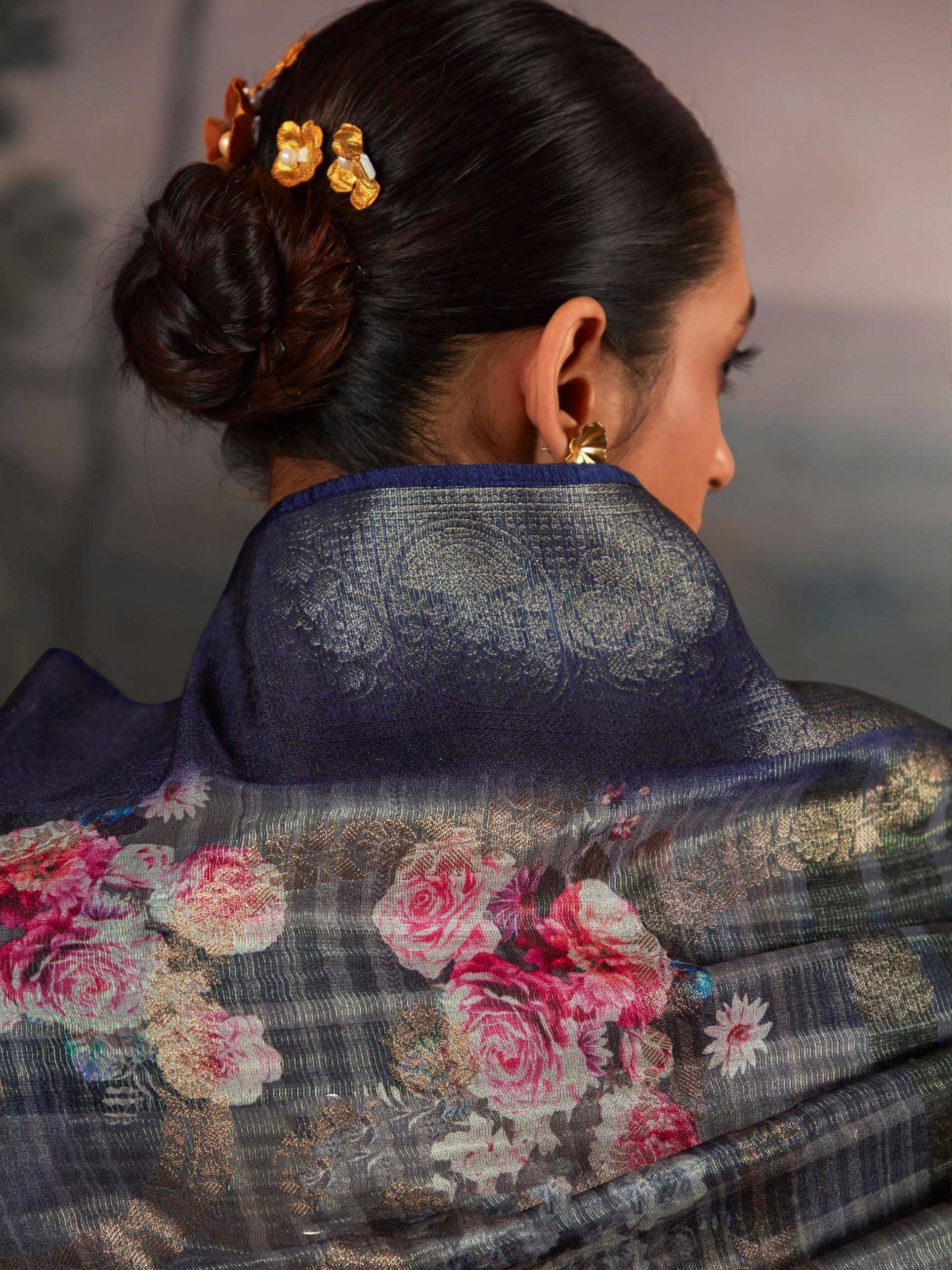 Woman in navy floral saree with gold embroidery, elegant bun hairstyle and gold hairpins