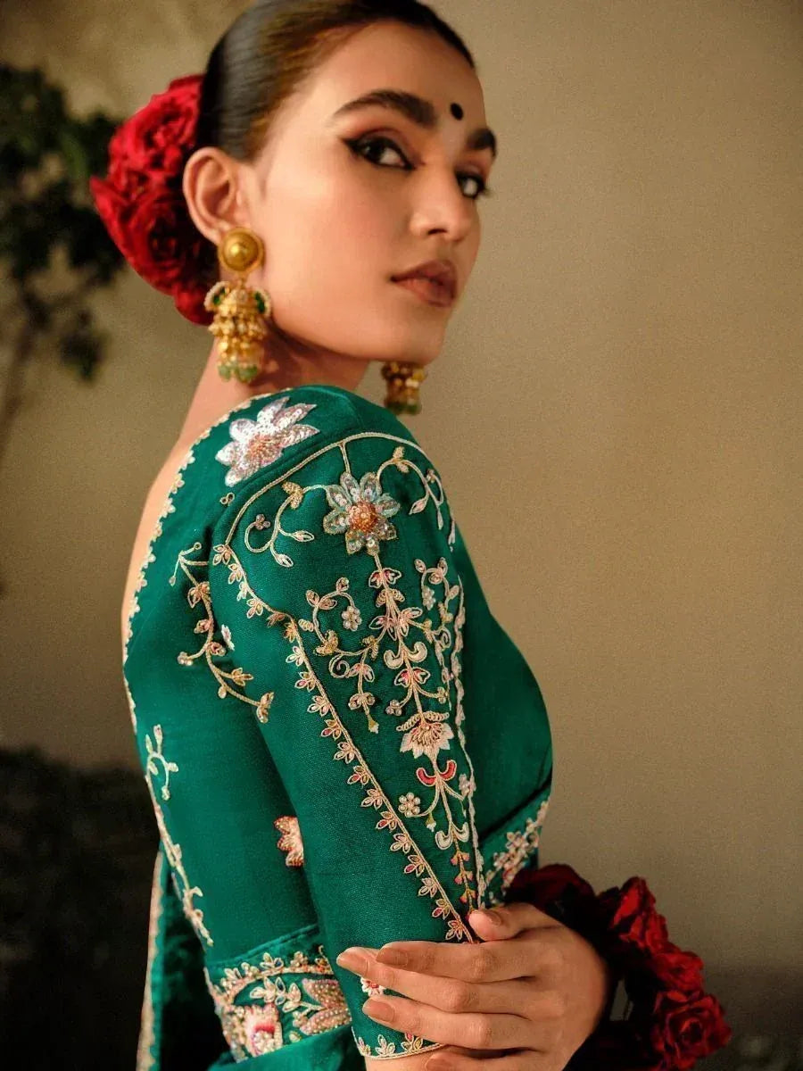 Emerald green embroidered ethnic blouse with floral detailing, gold jhumka earrings, and red rose hair accessory