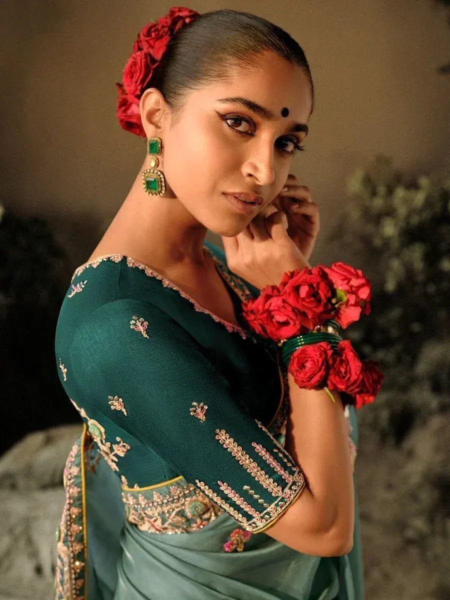 Elegant green saree with floral embroidery, red rose hair accessory, and emerald earrings