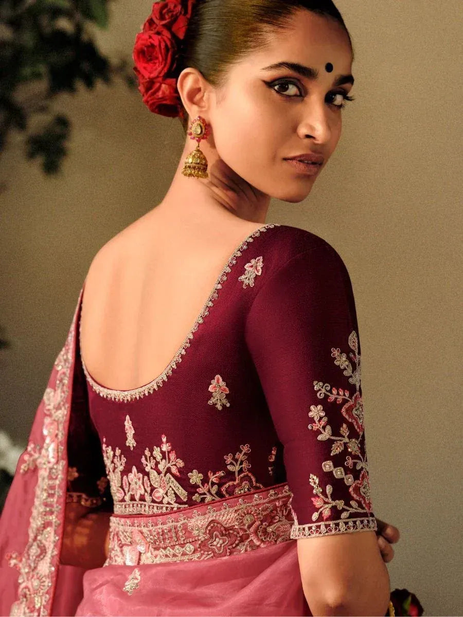 Maroon embroidered lehenga choli with floral detailing, gold jhumka earrings, and red rose hair accessory