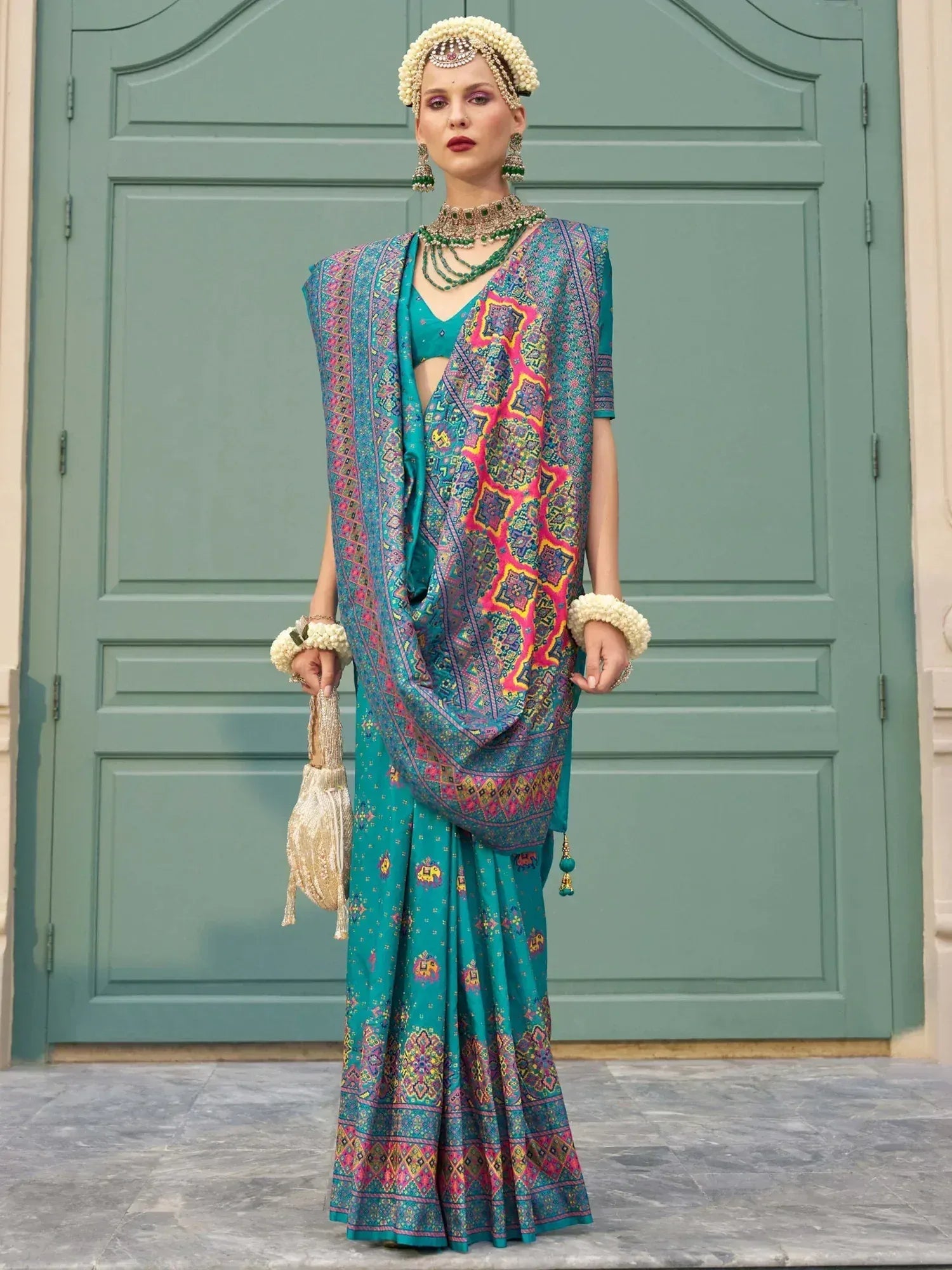 Teal printed saree with colorful geometric patterns, paired with matching blouse and traditional jewelry, perfect for ethnic occasions.