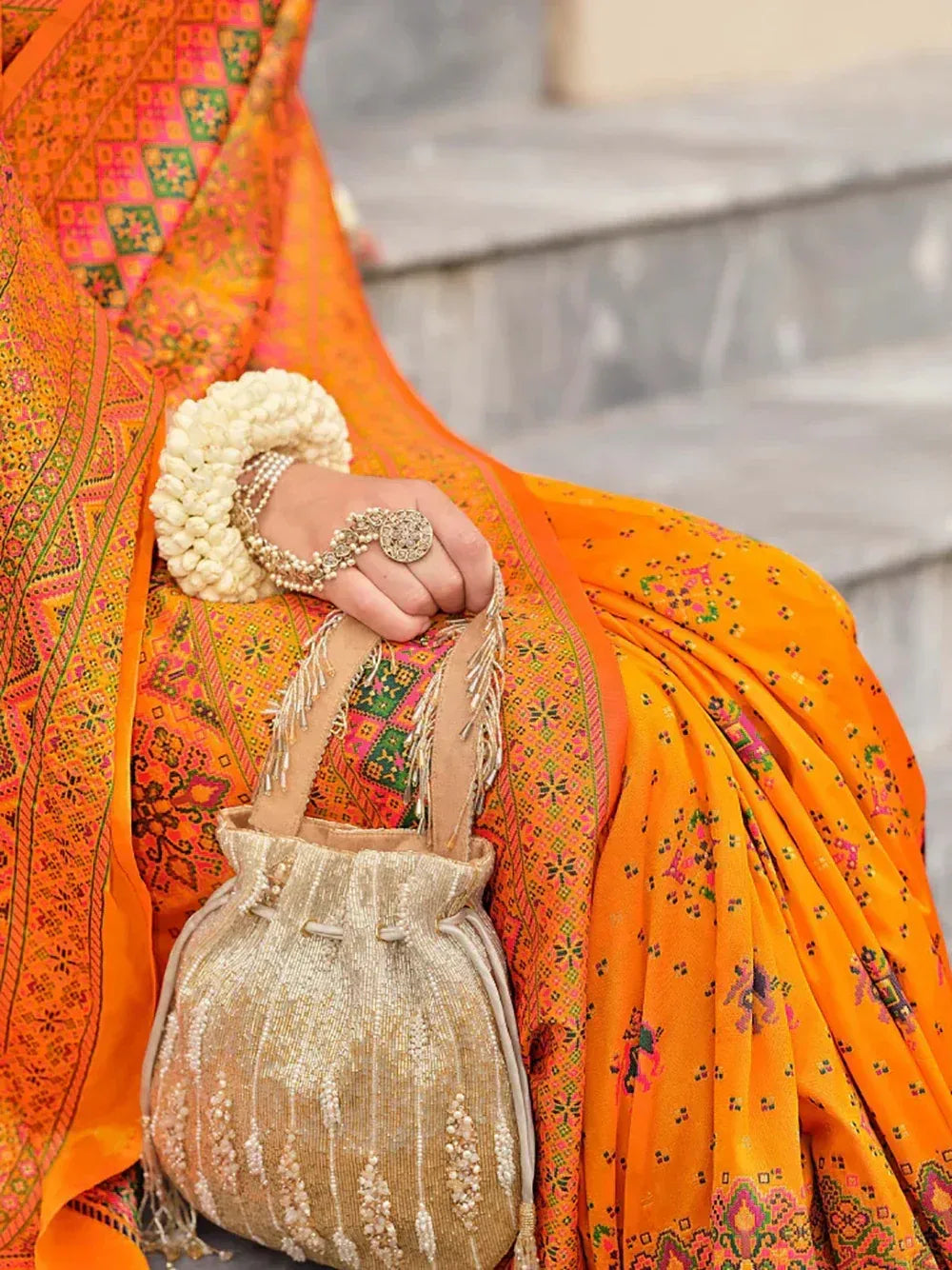 Vibrant orange ethnic saree with intricate embroidery, paired with floral bangles and a beaded potli bag.