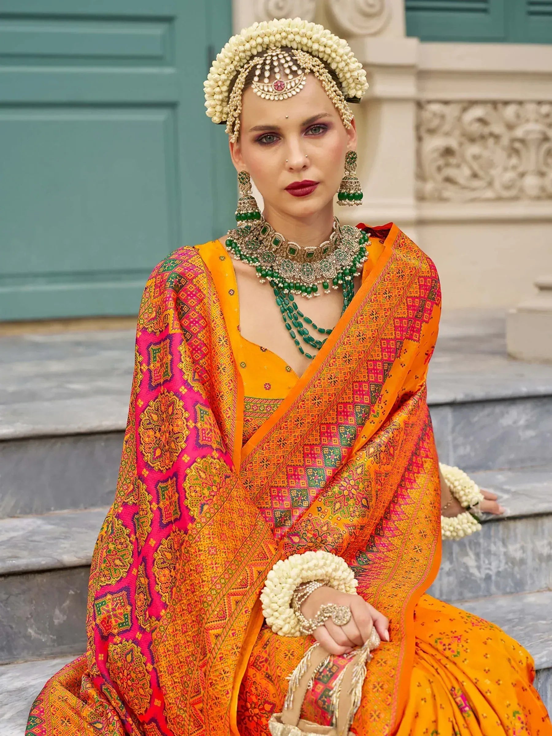 Vibrant orange and pink ethnic saree with floral jewelry, perfect for Indian weddings and festive occasions.