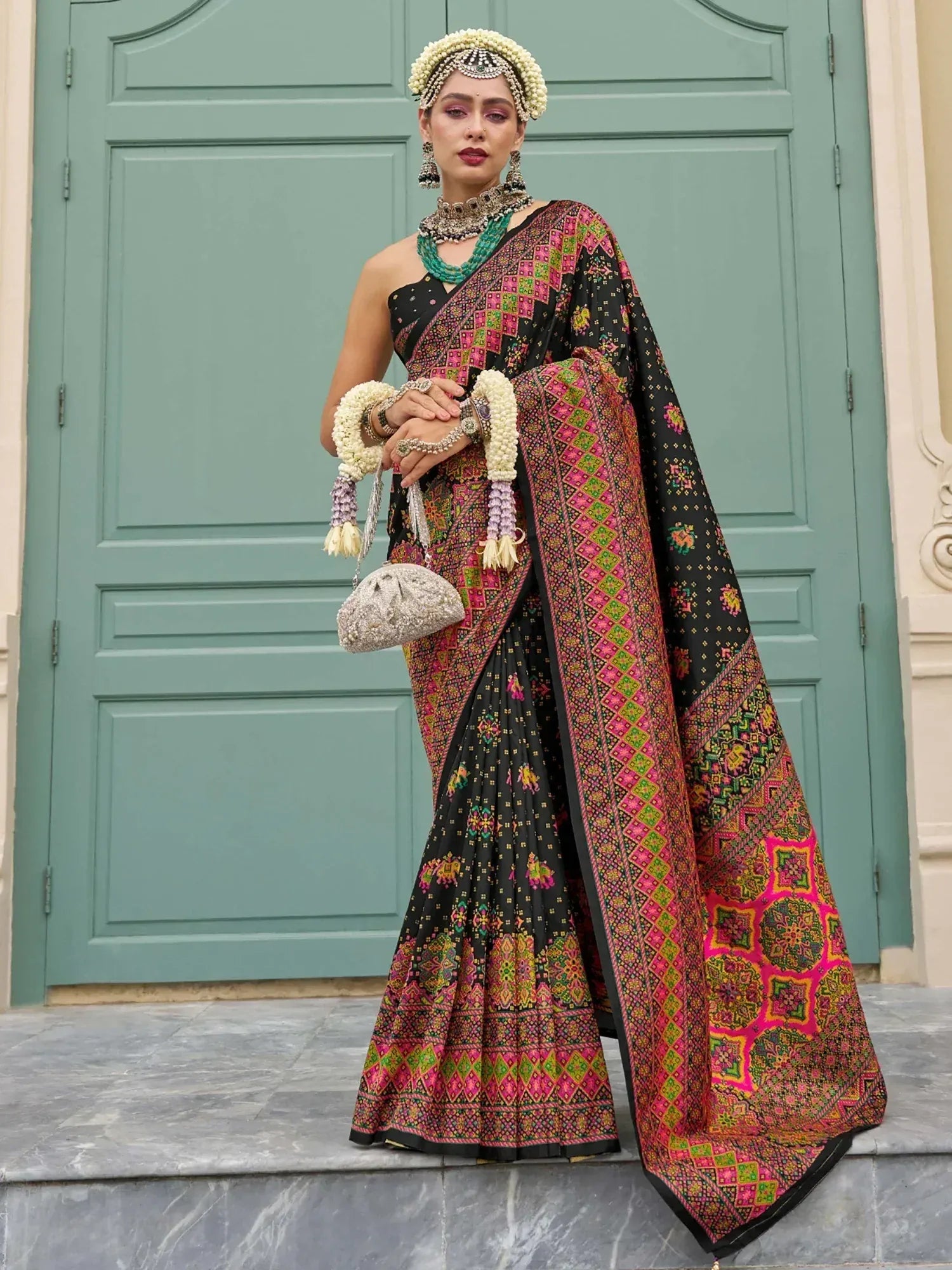 Woman in black and pink embroidered saree with floral jewelry, perfect for Indian ethnic wear occasions.