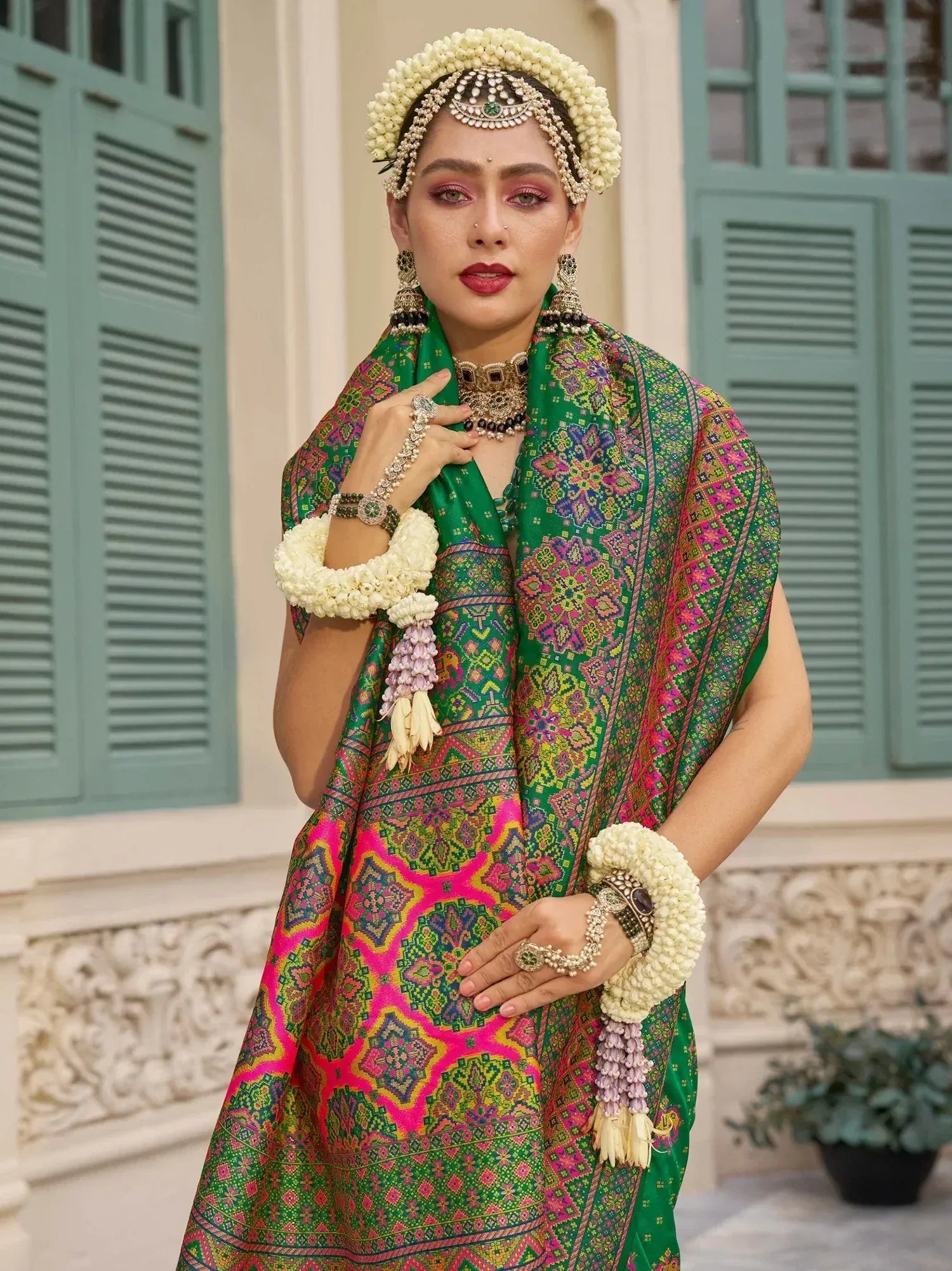 Woman in vibrant green and pink ethnic gown with floral jewelry, traditional Indian attire