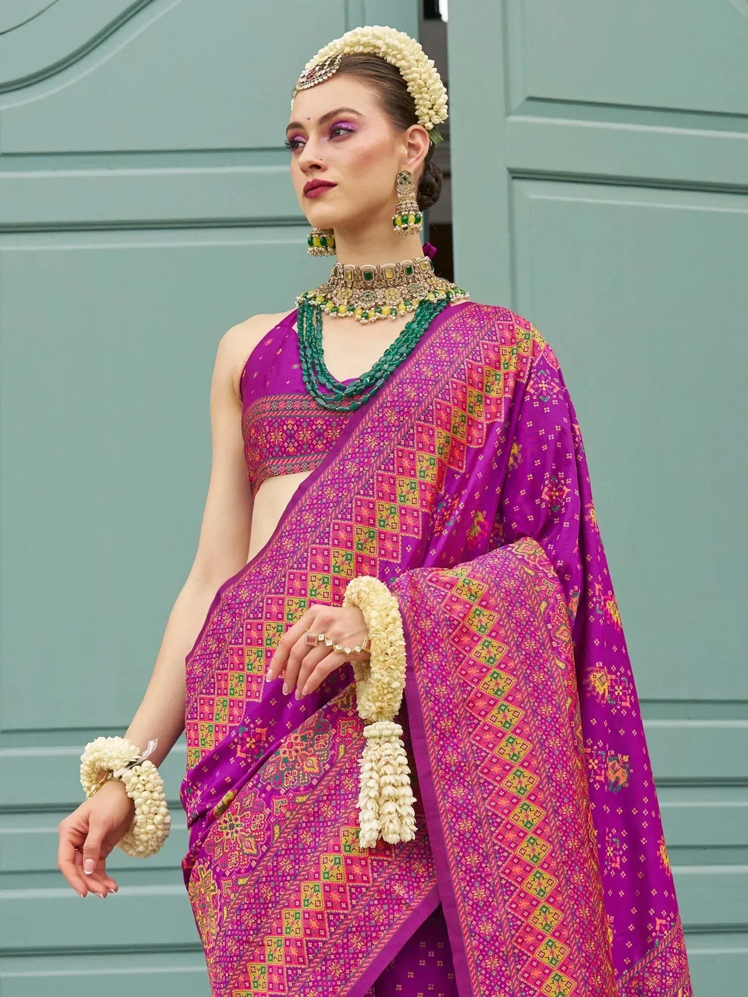 Vibrant purple ethnic saree with intricate geometric print, paired with floral jewelry and traditional headpiece