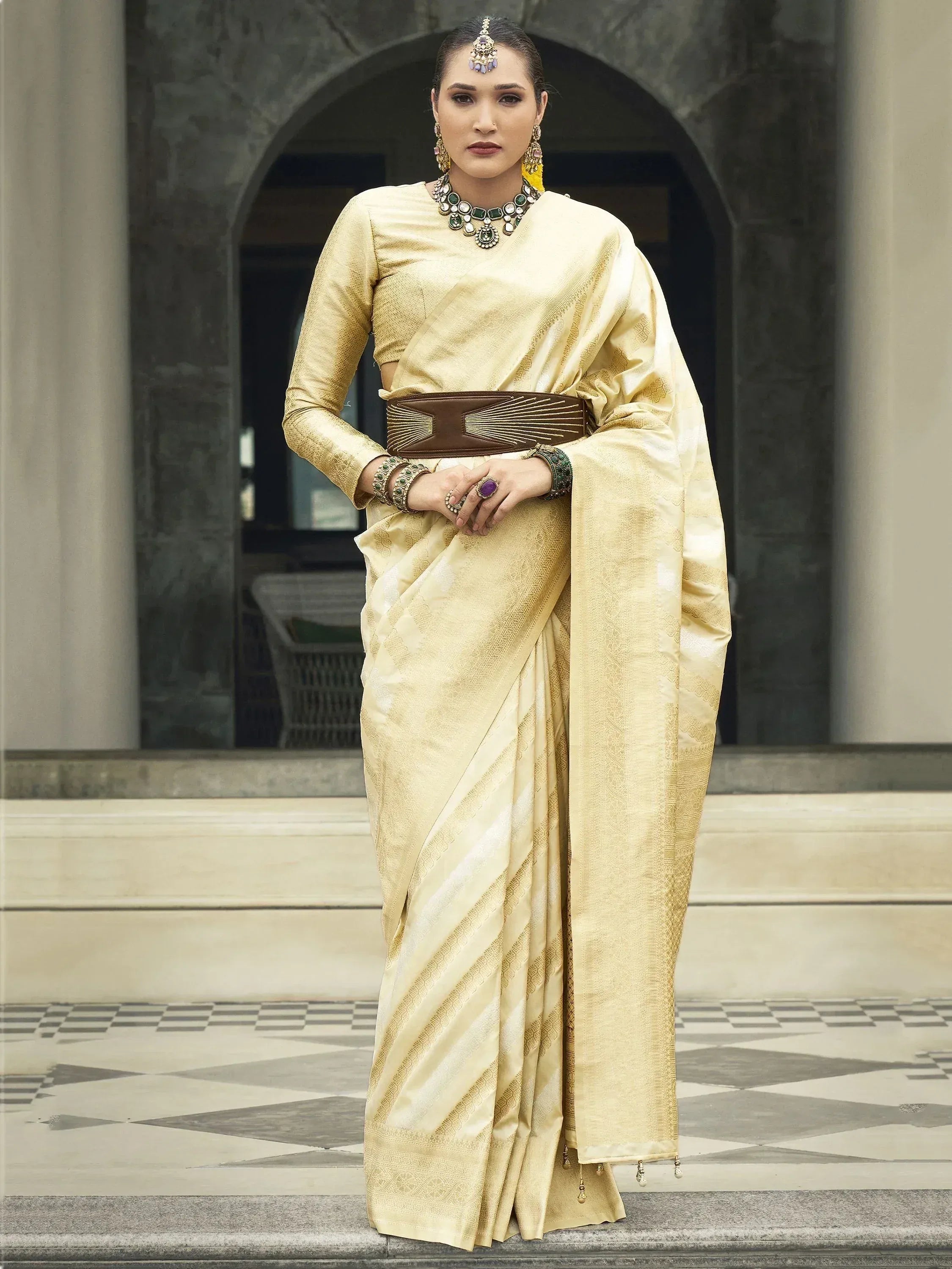 Elegant gold saree with intricate patterns, paired with statement jewelry and a brown belt, perfect for Indian ethnic occasions.