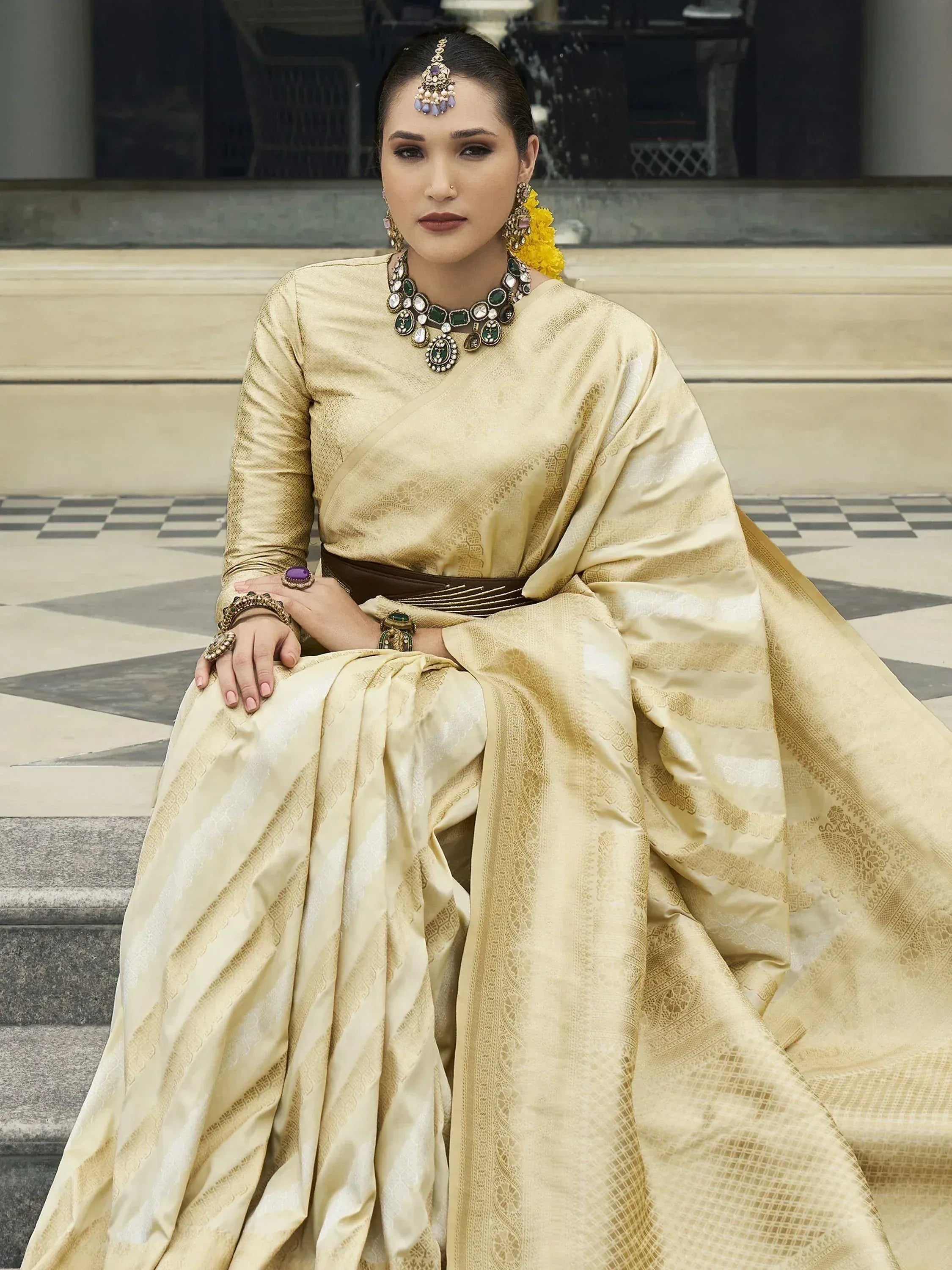 Elegant woman in golden designer saree with intricate patterns, traditional jewelry, and floral hair accessory