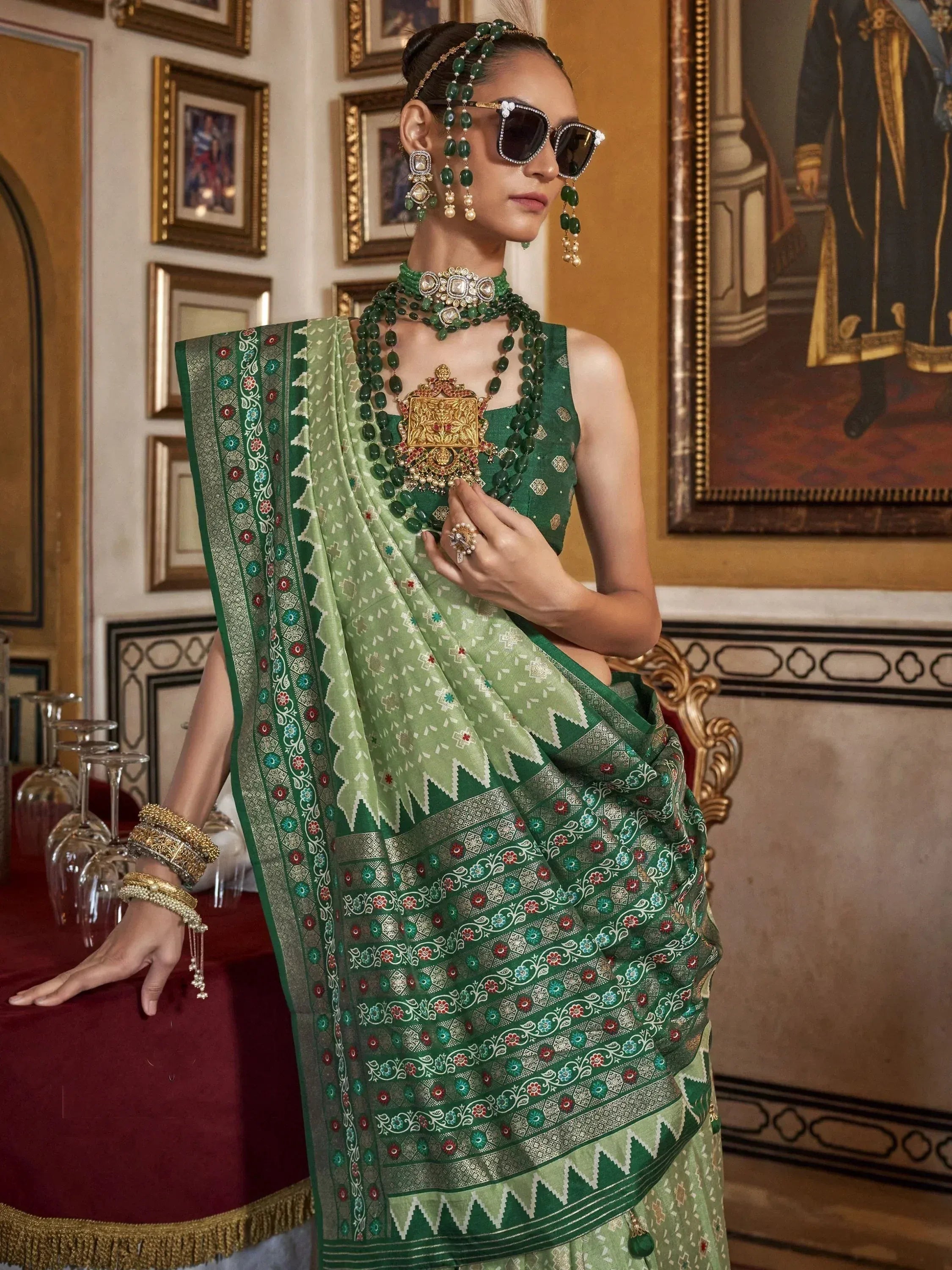 Elegant green designer saree with intricate embroidery, paired with traditional jewelry and sunglasses for a modern ethnic look.
