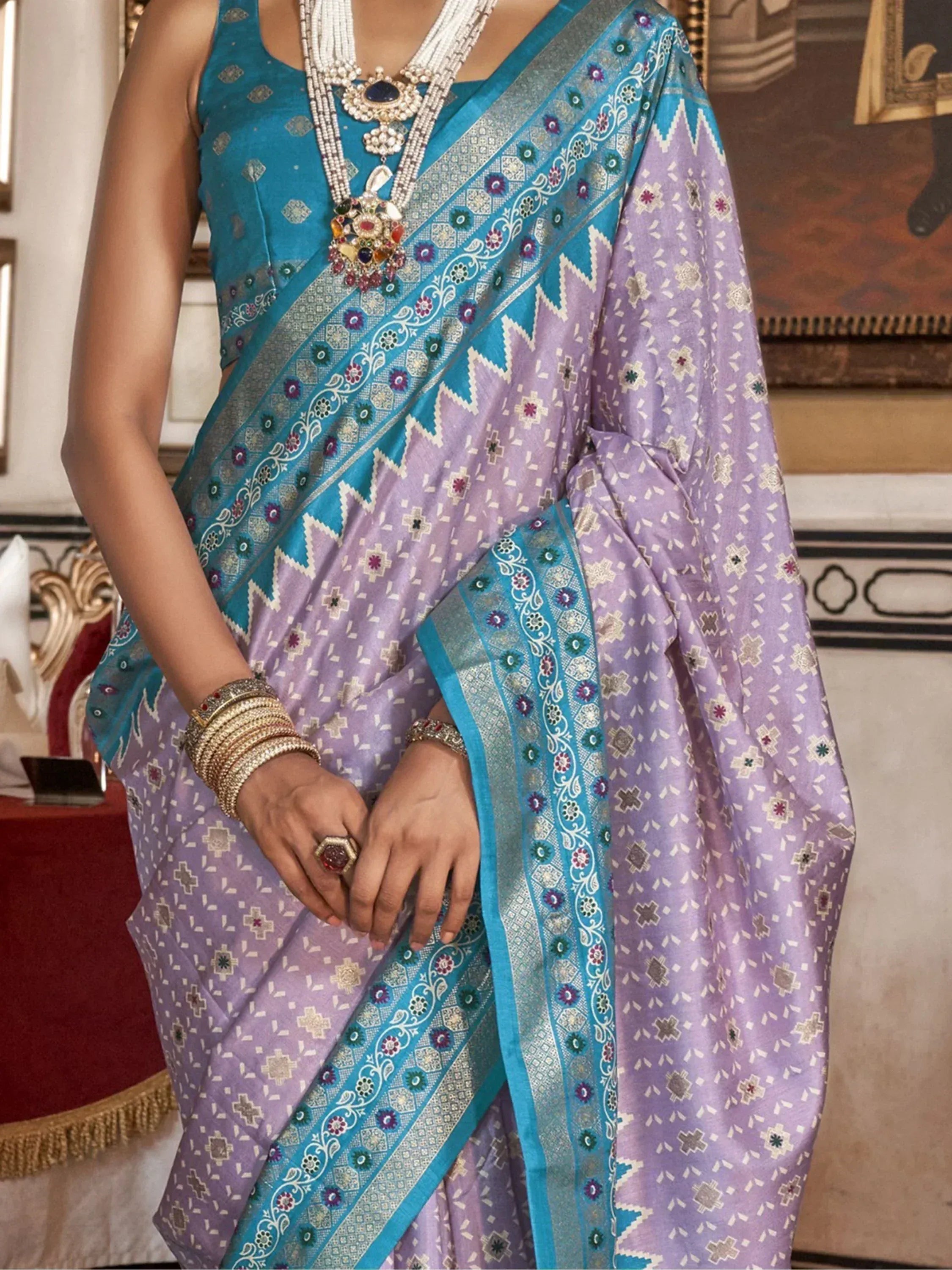 Purple and teal designer saree with intricate floral border, paired with traditional jewelry for ethnic wear.