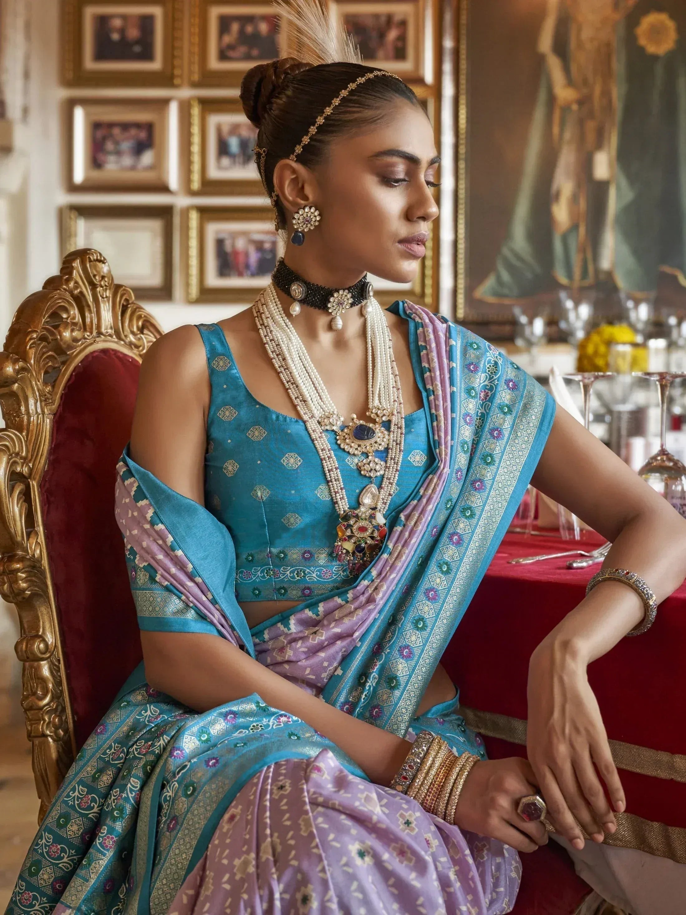 Elegant woman in blue and lavender designer saree with intricate embroidery, traditional jewelry, seated on ornate chair