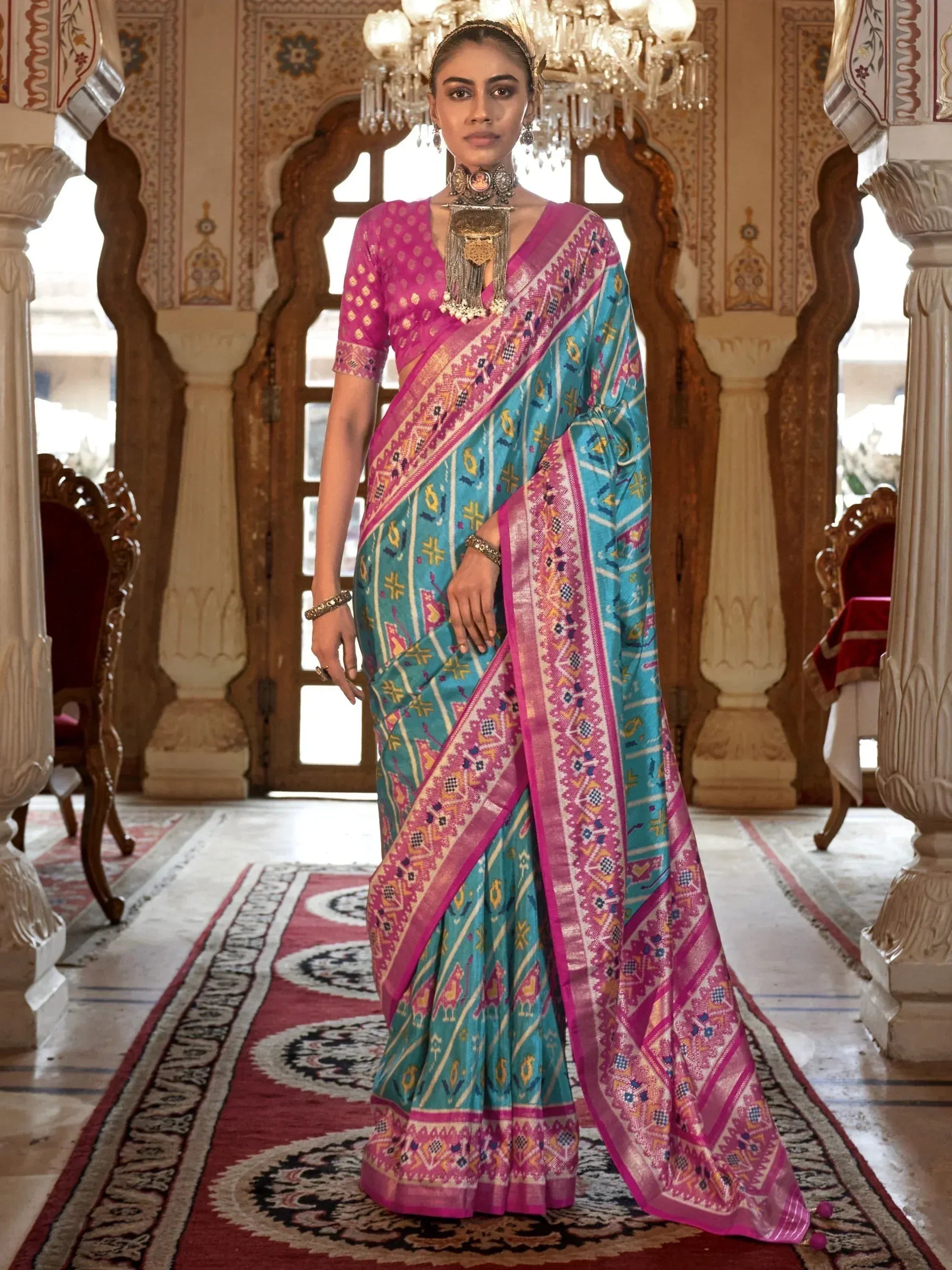 Woman in vibrant turquoise and pink ethnic saree with intricate patterns, traditional jewelry, palace setting