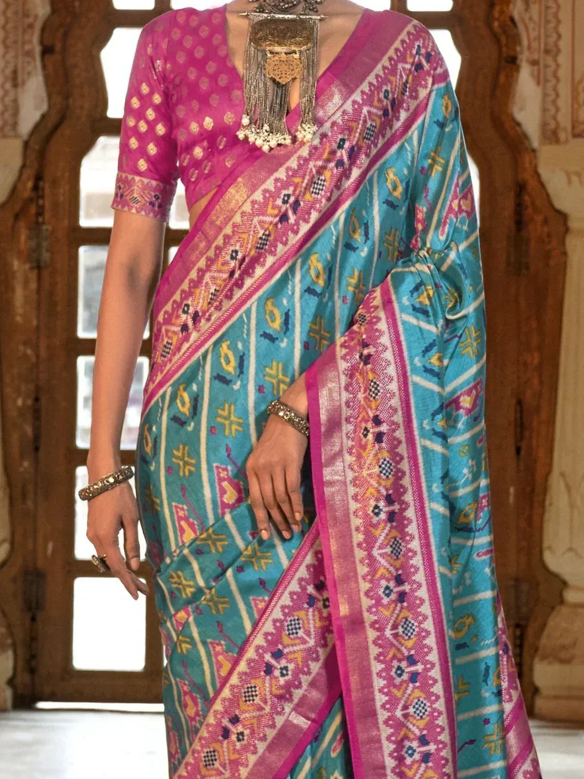 Turquoise and pink ethnic saree with intricate geometric patterns and matching blouse, styled with traditional jewelry.
