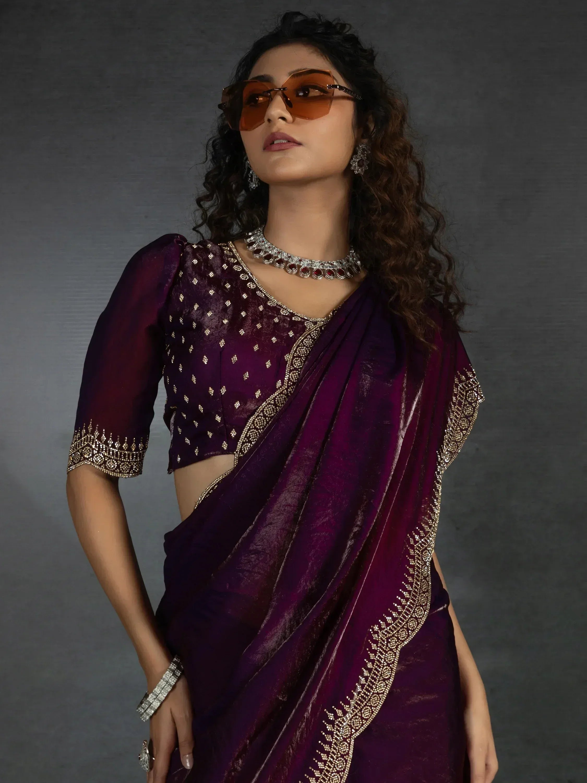 Elegant purple saree with gold embroidery, paired with statement jewelry and stylish sunglasses