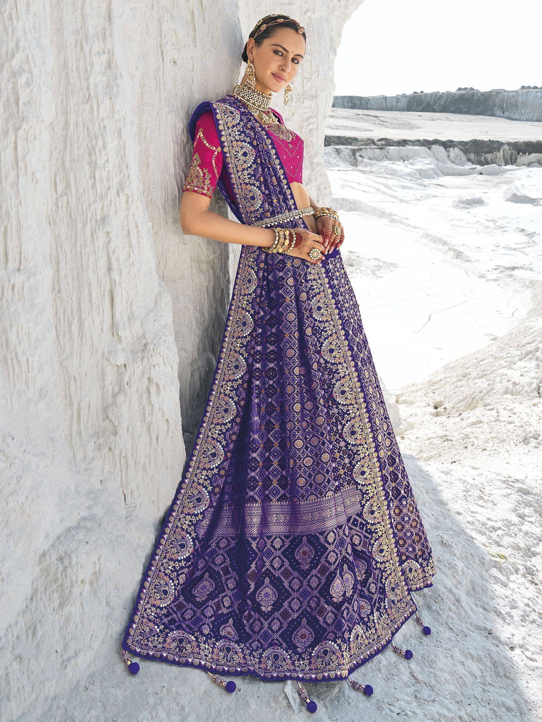 Woman in purple embroidered lehenga choli with gold detailing, posing against white rock formation