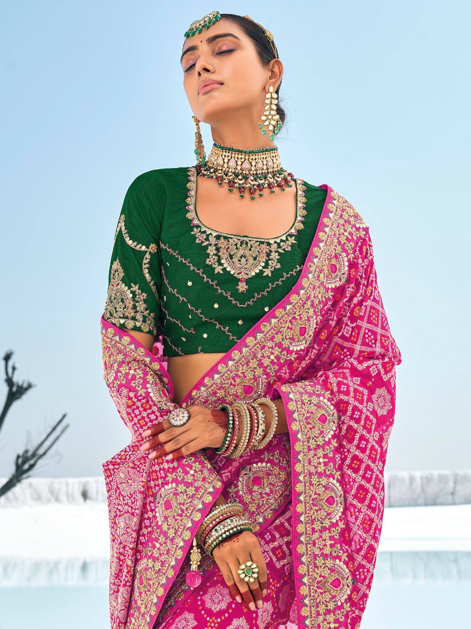 Woman in vibrant pink and green embroidered saree with gold jewelry, perfect for Indian ethnic occasions