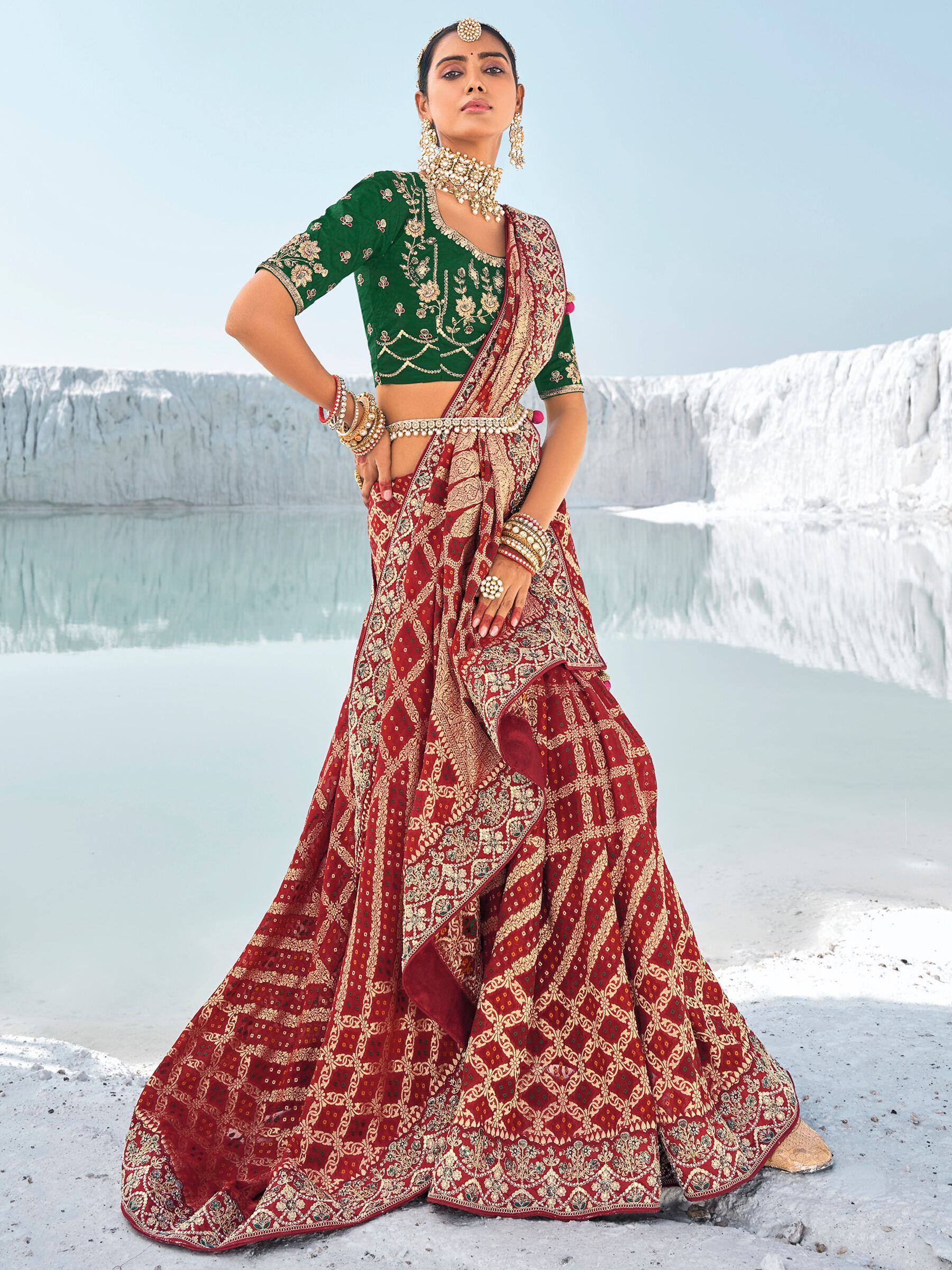Woman in red and green embroidered lehenga choli with gold jewelry, standing by white terraces