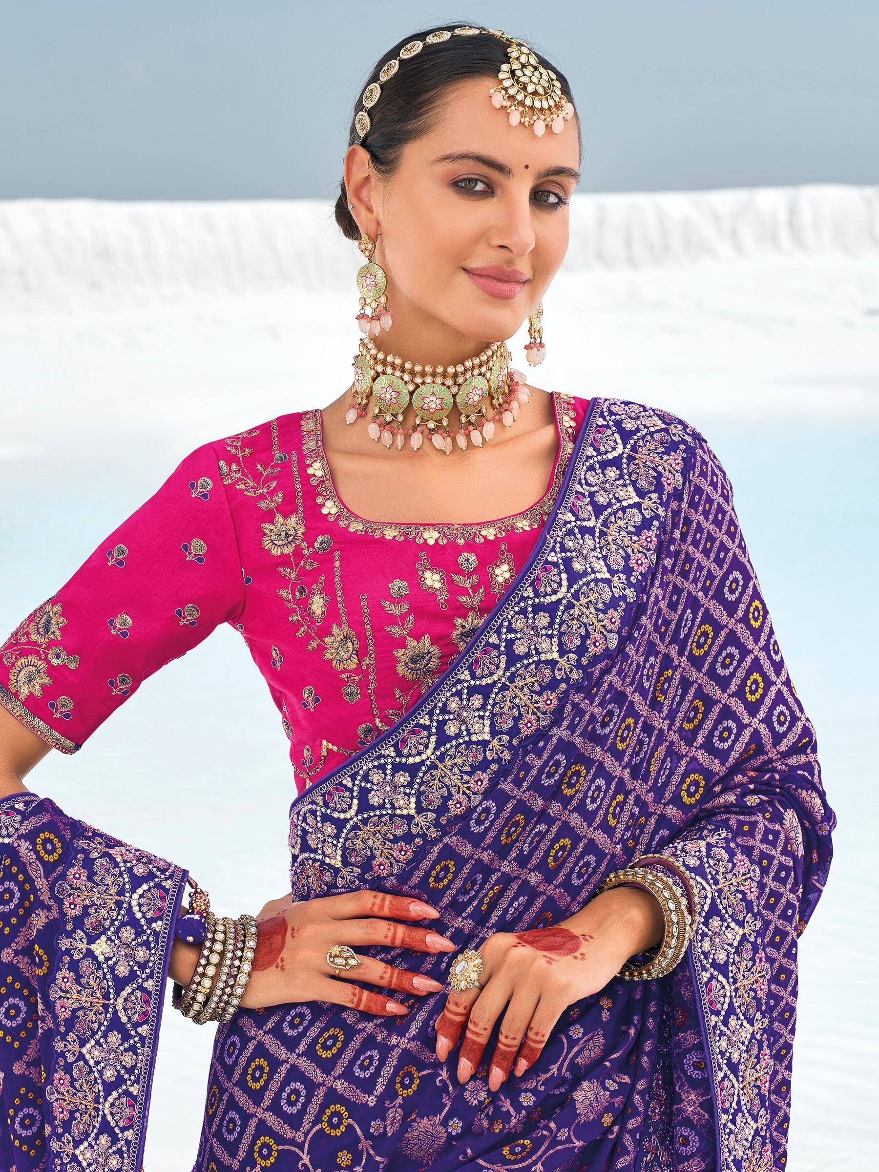 Woman in vibrant pink and purple embroidered Indian saree with traditional jewelry and henna hands