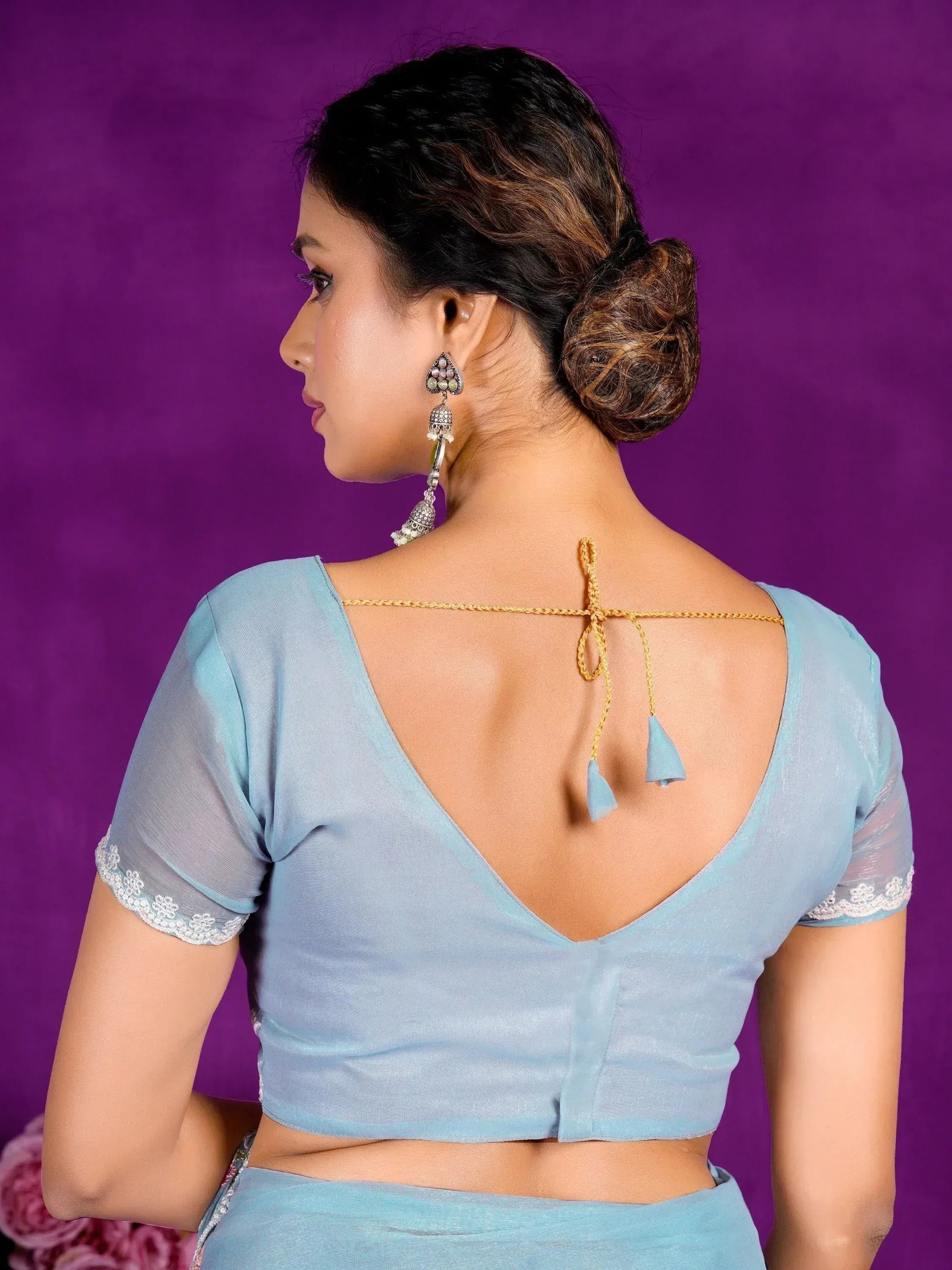 Light blue saree blouse with open back, lace sleeves, and tassel ties, paired with ethnic jewelry.