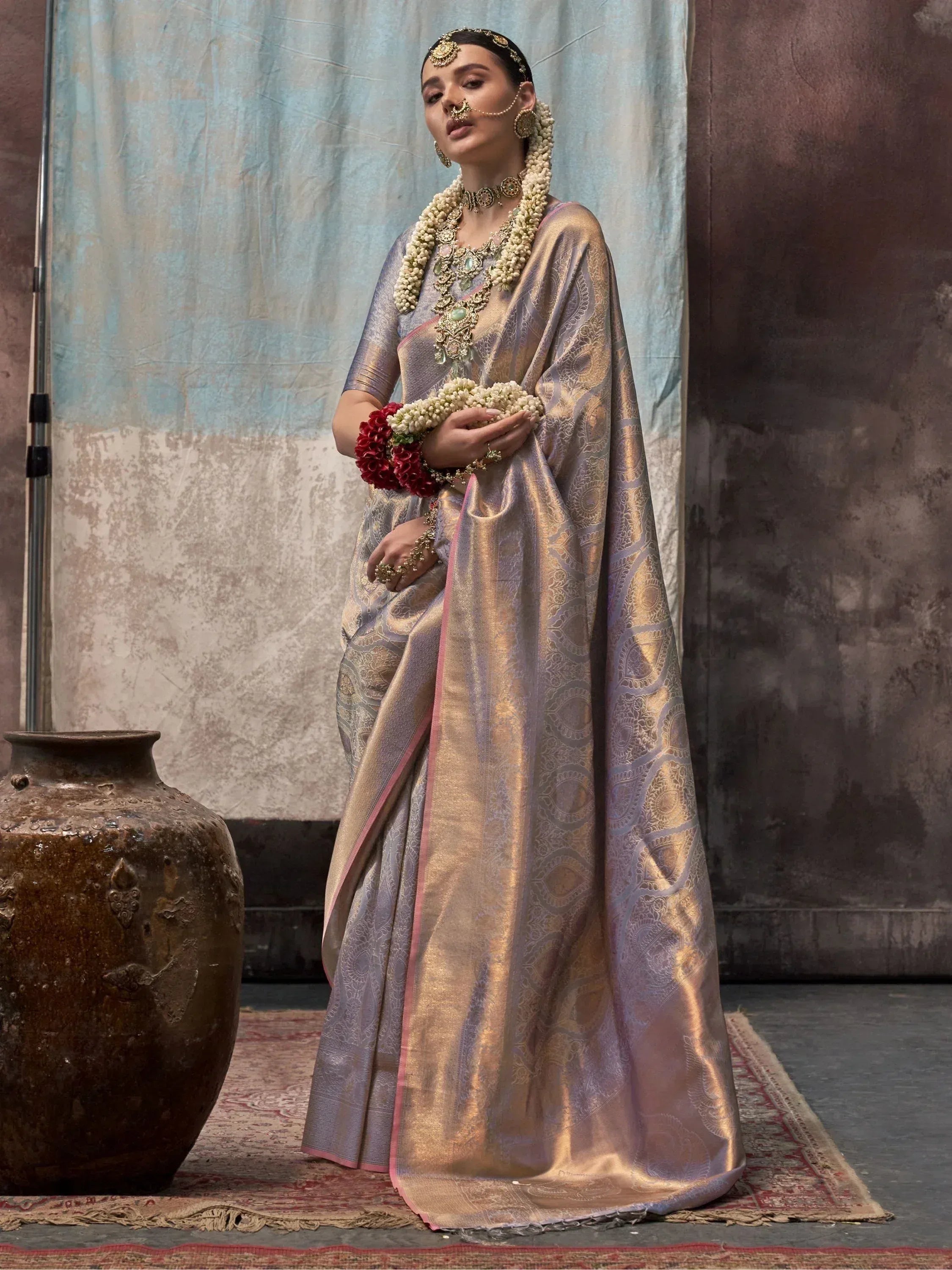 Elegant woman in lavender and gold designer saree with intricate embroidery, traditional jewelry, and floral garlands.