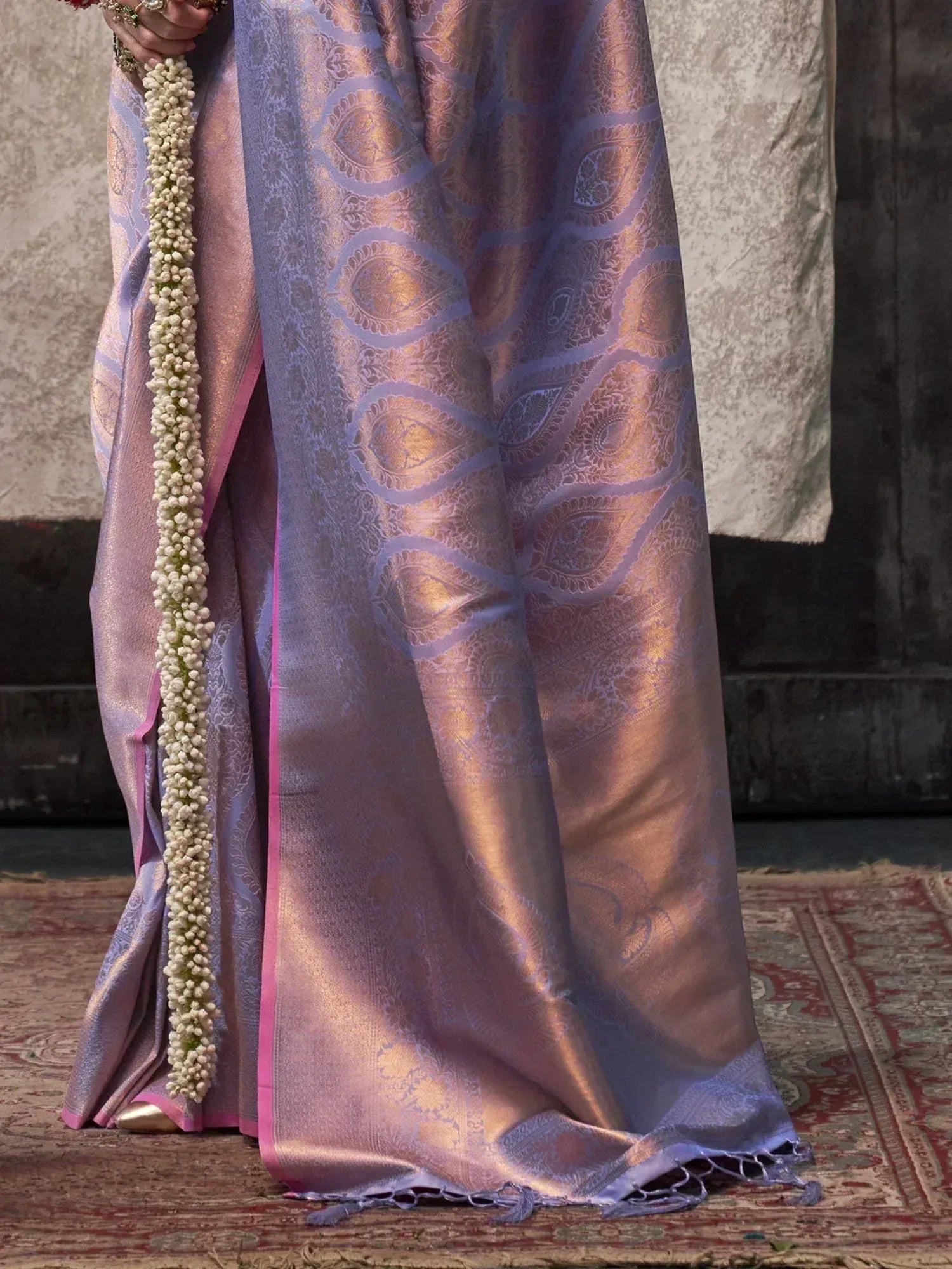 Lavender and gold paisley saree with pink border, held with floral garland, ethnic Indian wear