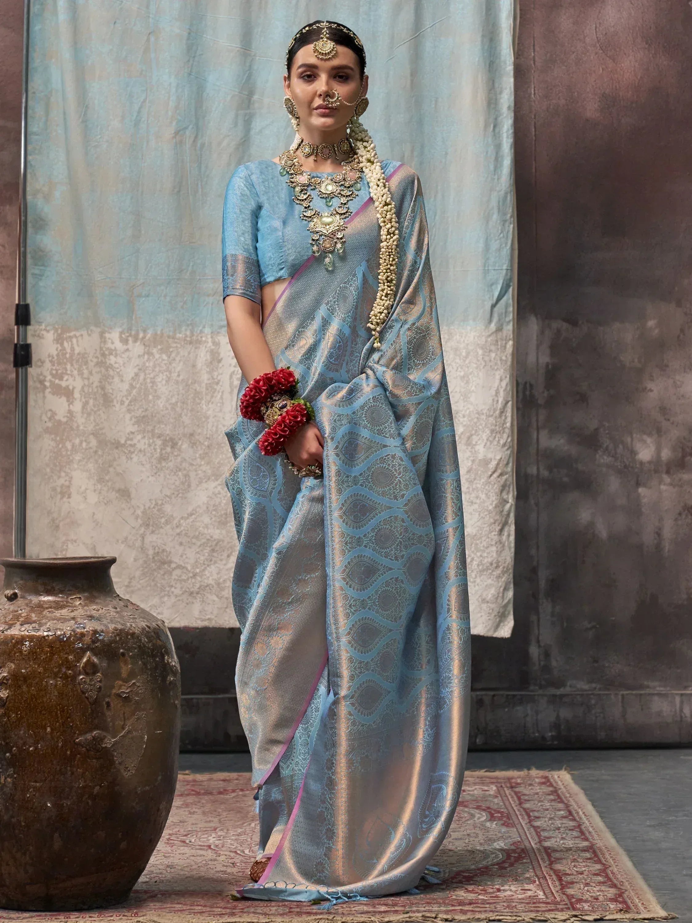 Woman in blue designer saree with gold embroidery, traditional jewelry, and floral accessories for ethnic wear.