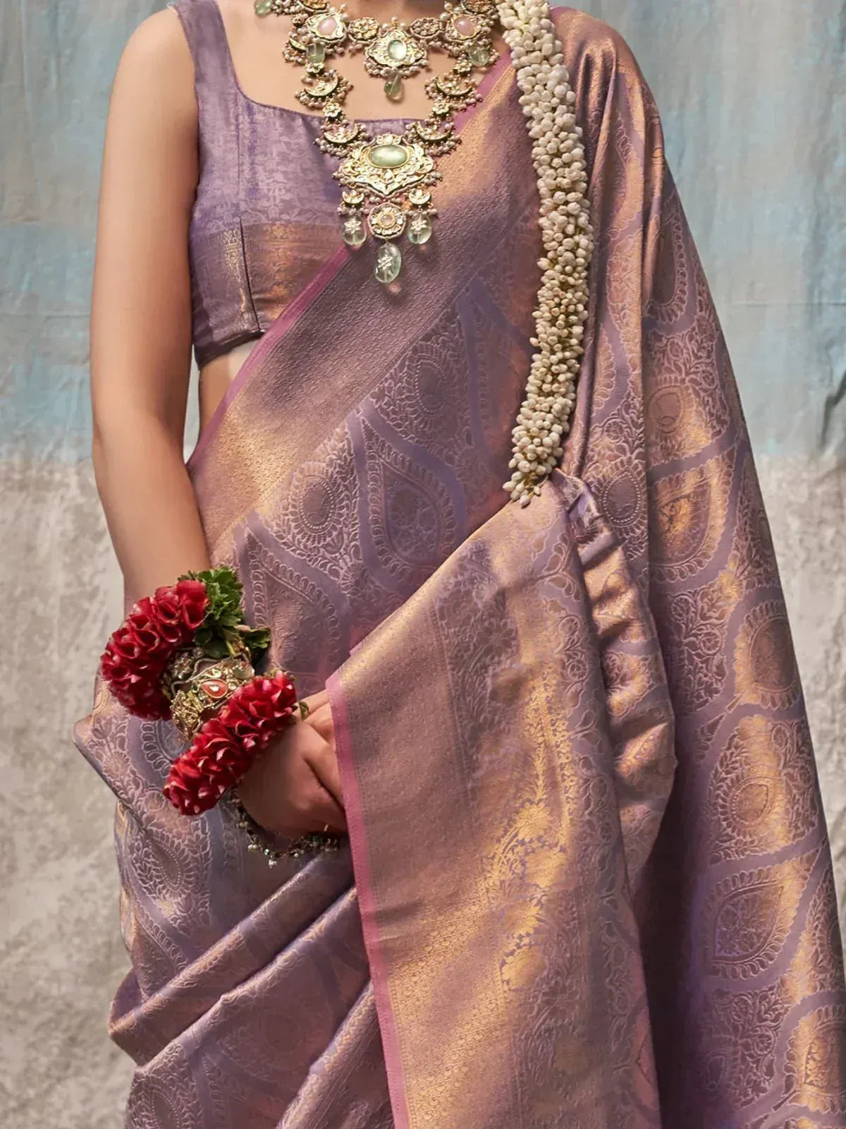 Purple and gold designer saree with intricate paisley patterns, paired with traditional jewelry and floral accessories.