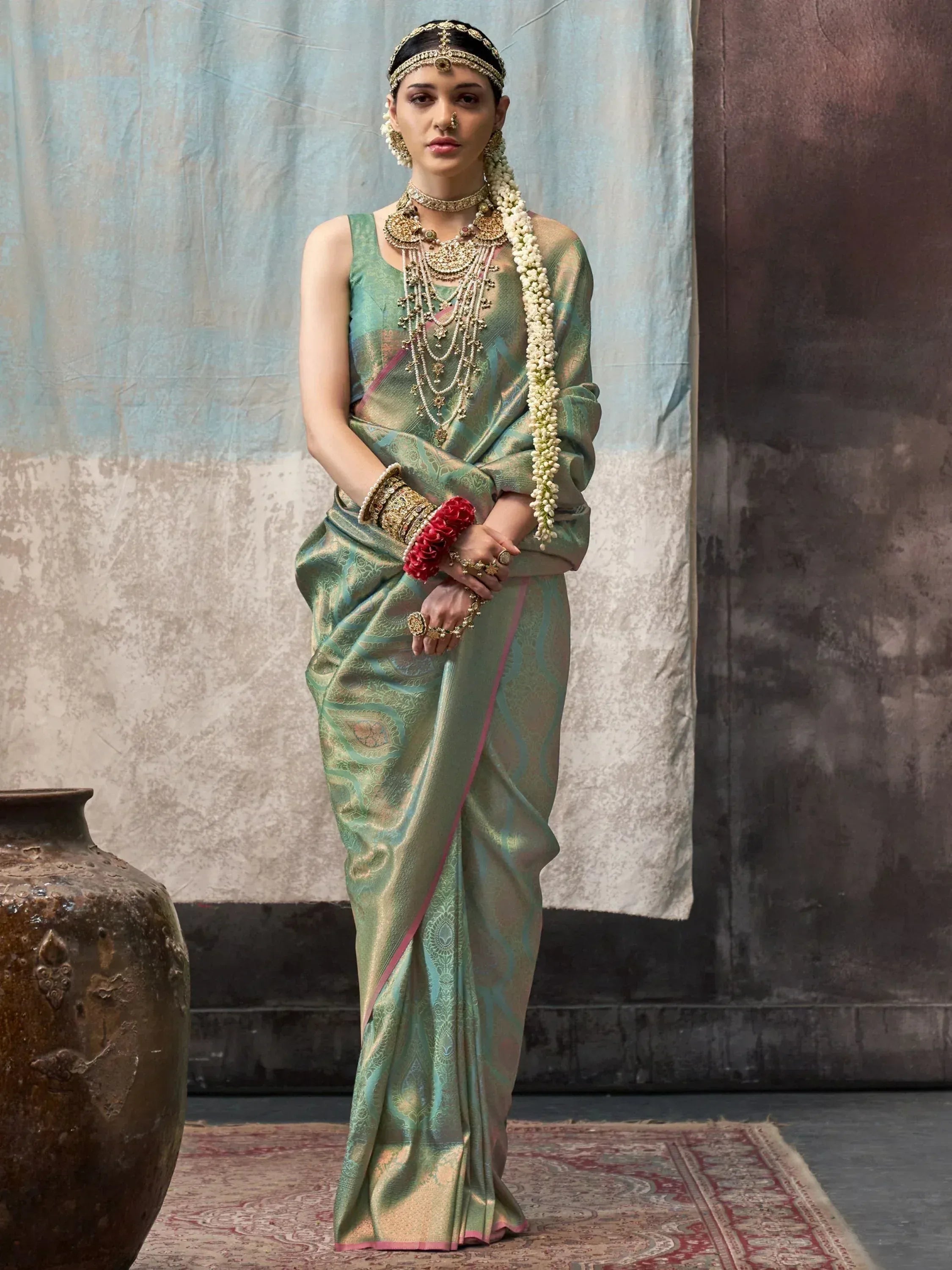 Woman in green designer saree with gold embroidery, traditional Indian jewelry, and floral garland