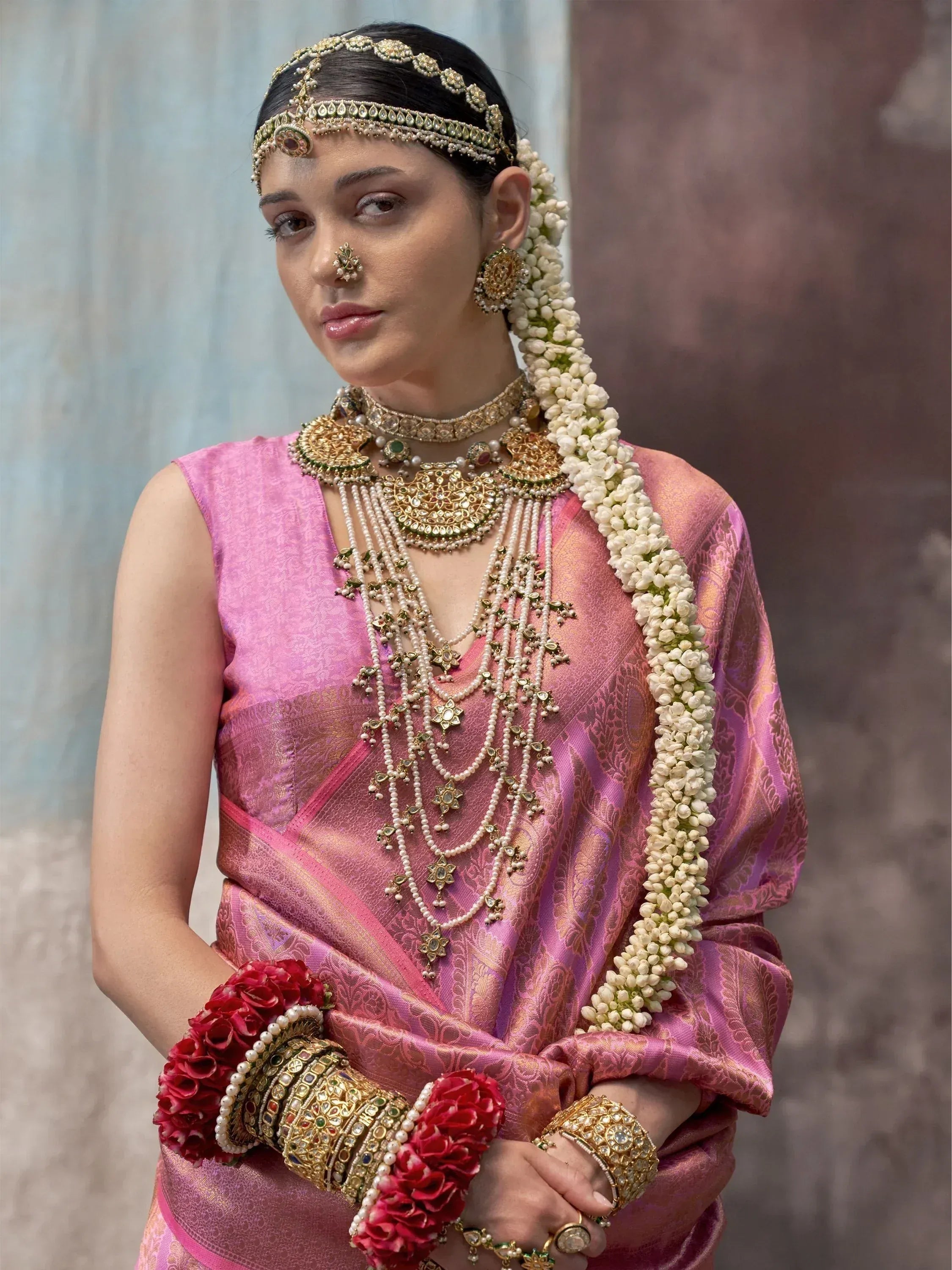 Woman in pink Indian bridal saree with gold jewelry and floral accessories