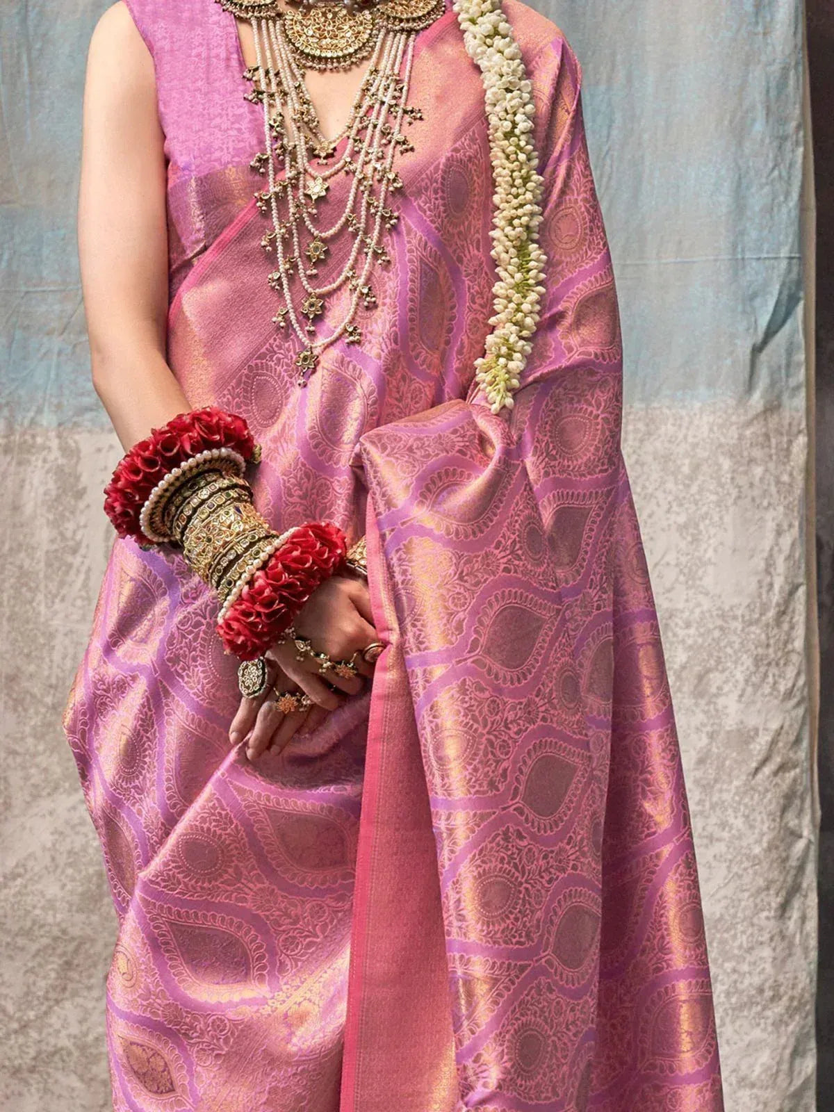 Pink designer saree with gold paisley weave, temple jewelry, and floral garland for Indian ethnic wear
