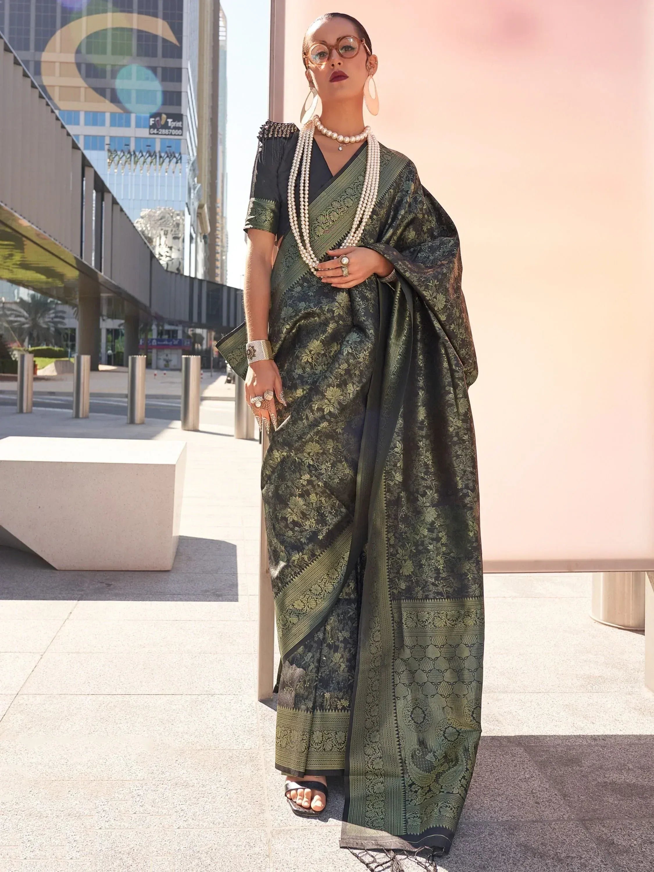 Woman in elegant dark green floral saree with gold border, styled with pearl necklace and modern accessories for ethnic wear.