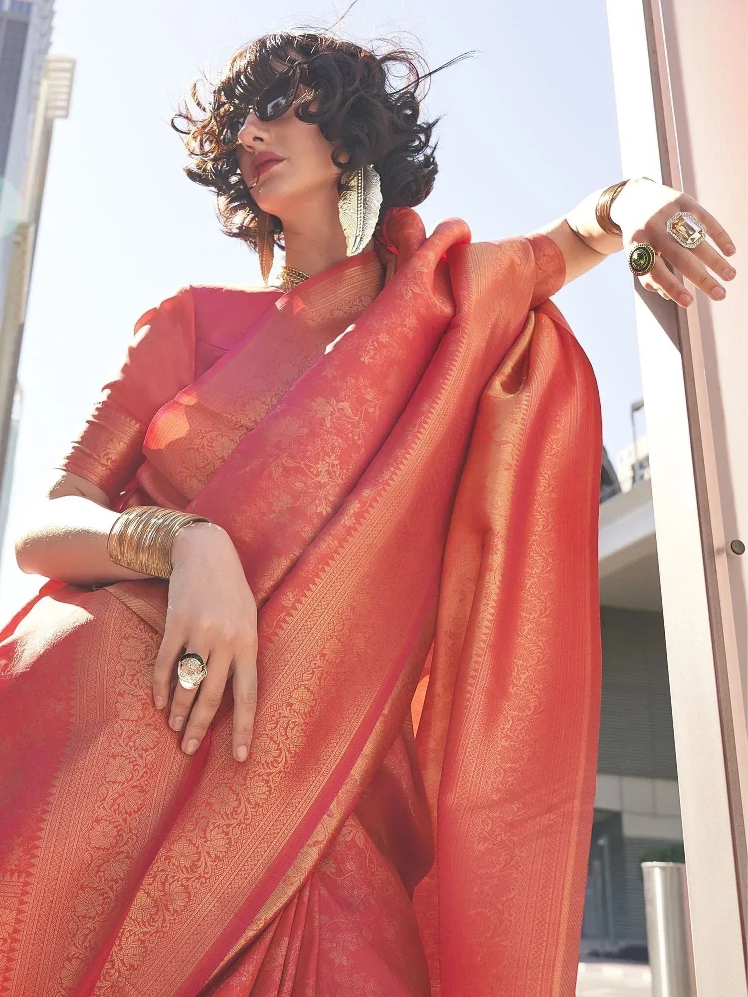 Woman in coral designer saree with gold embroidery, styled with statement jewelry for ethnic wear