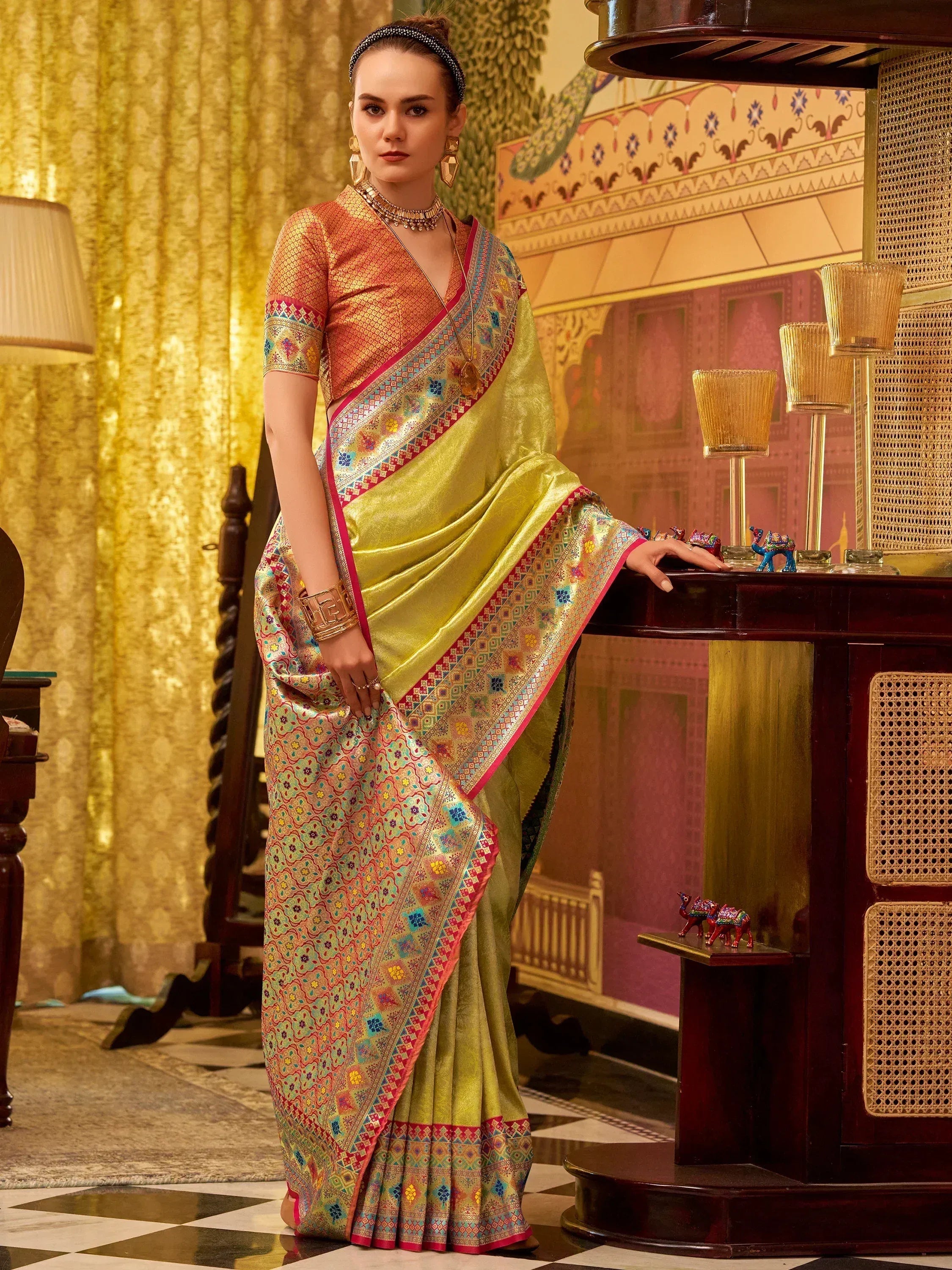 Elegant woman in vibrant yellow saree with intricate embroidery and colorful border, styled with traditional jewelry.
