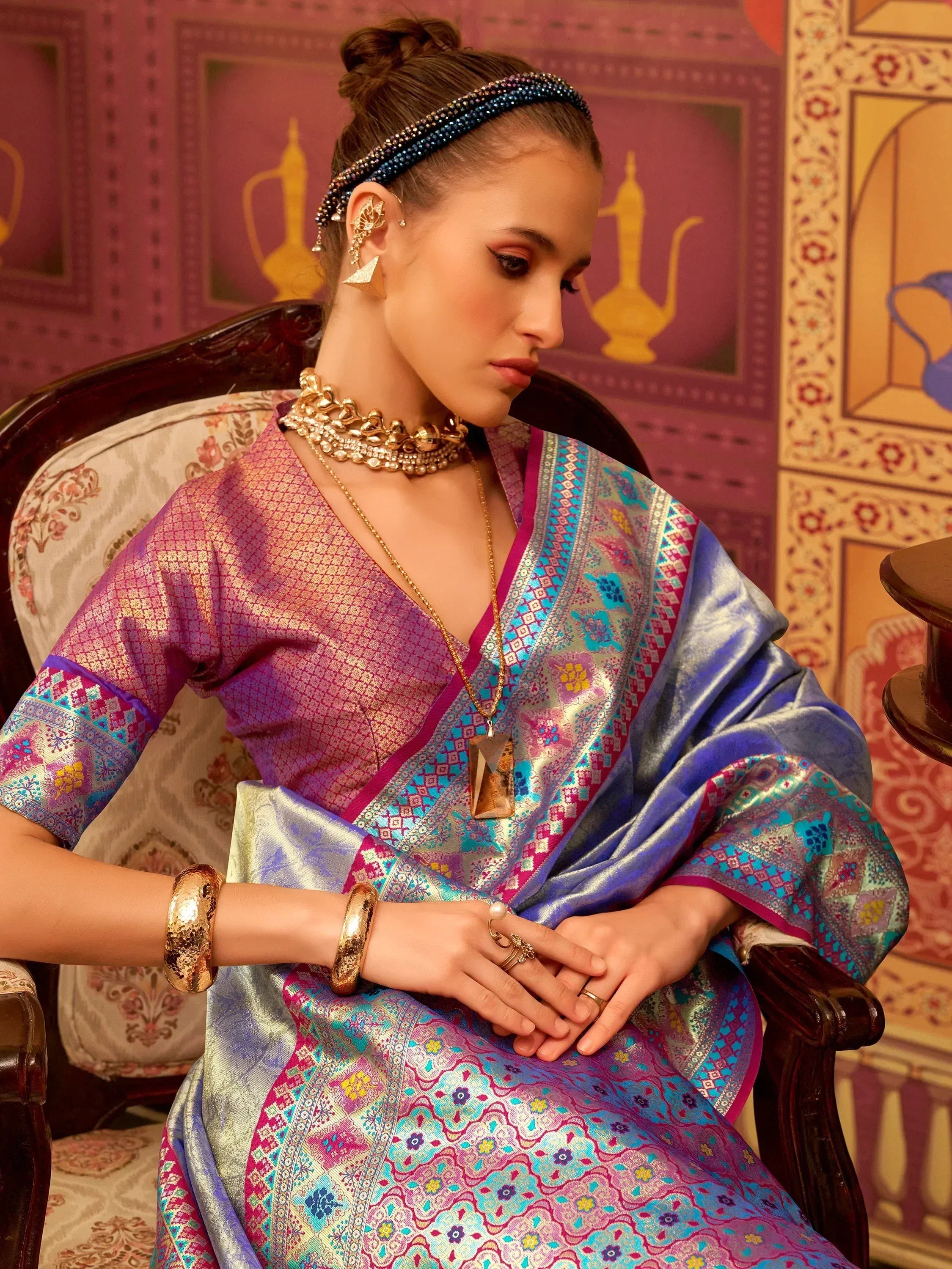 Elegant woman in vibrant purple and blue ethnic saree with intricate patterns and gold jewelry