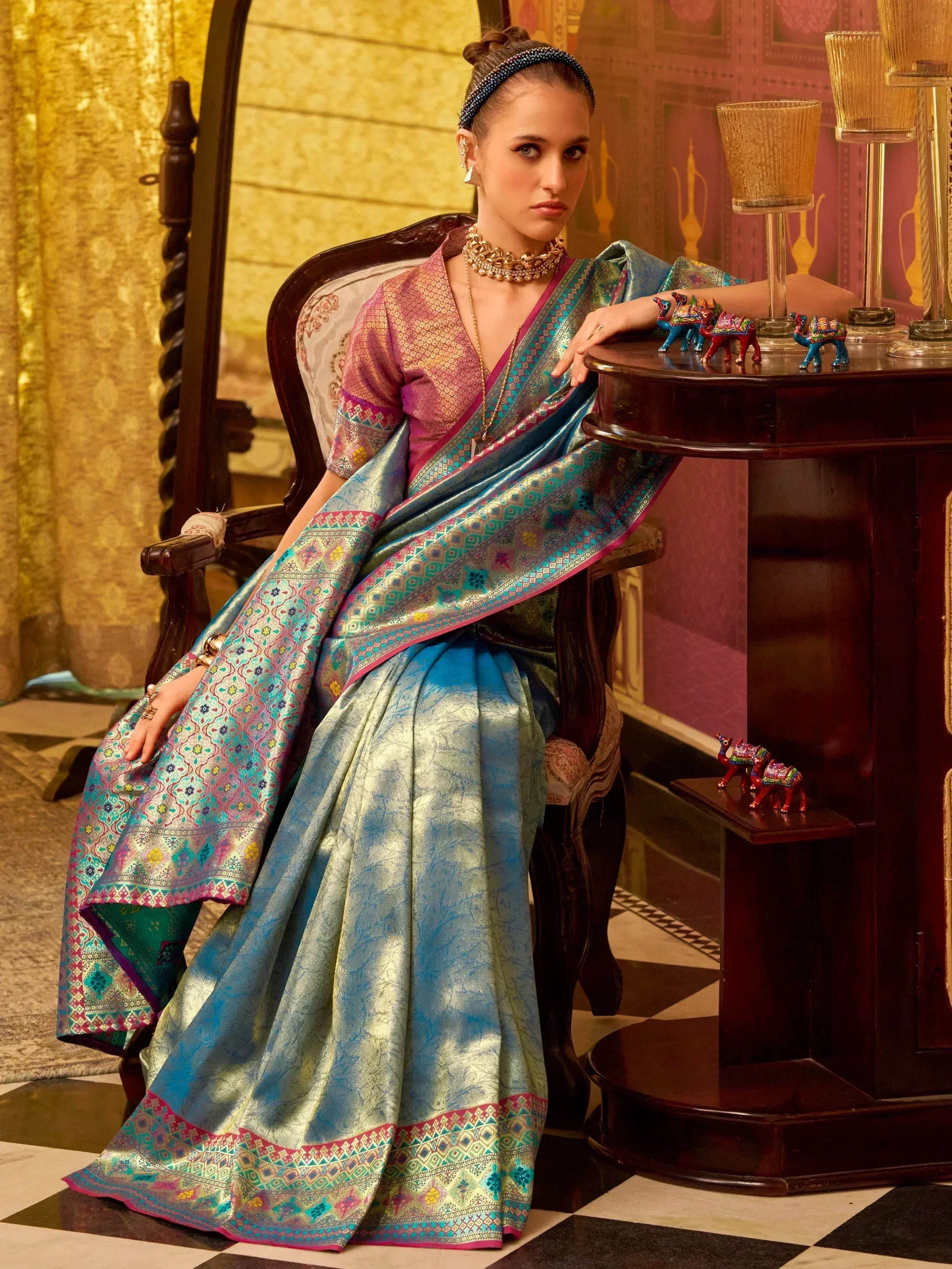 Elegant woman in blue and pink designer saree with intricate patterns, styled with traditional jewelry.