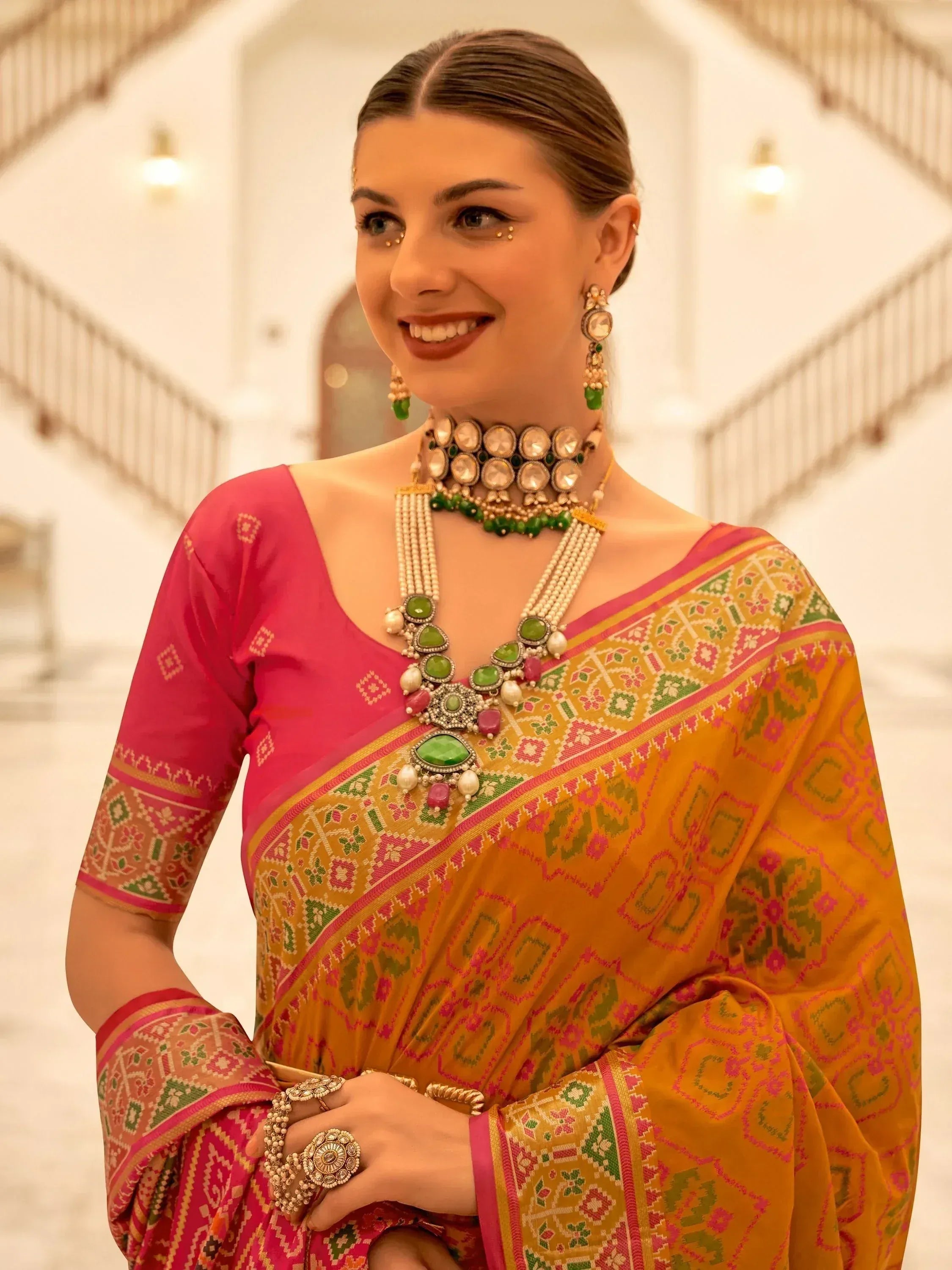 Woman in vibrant Indian saree with pink blouse, green and gold jewelry, traditional ethnic wear