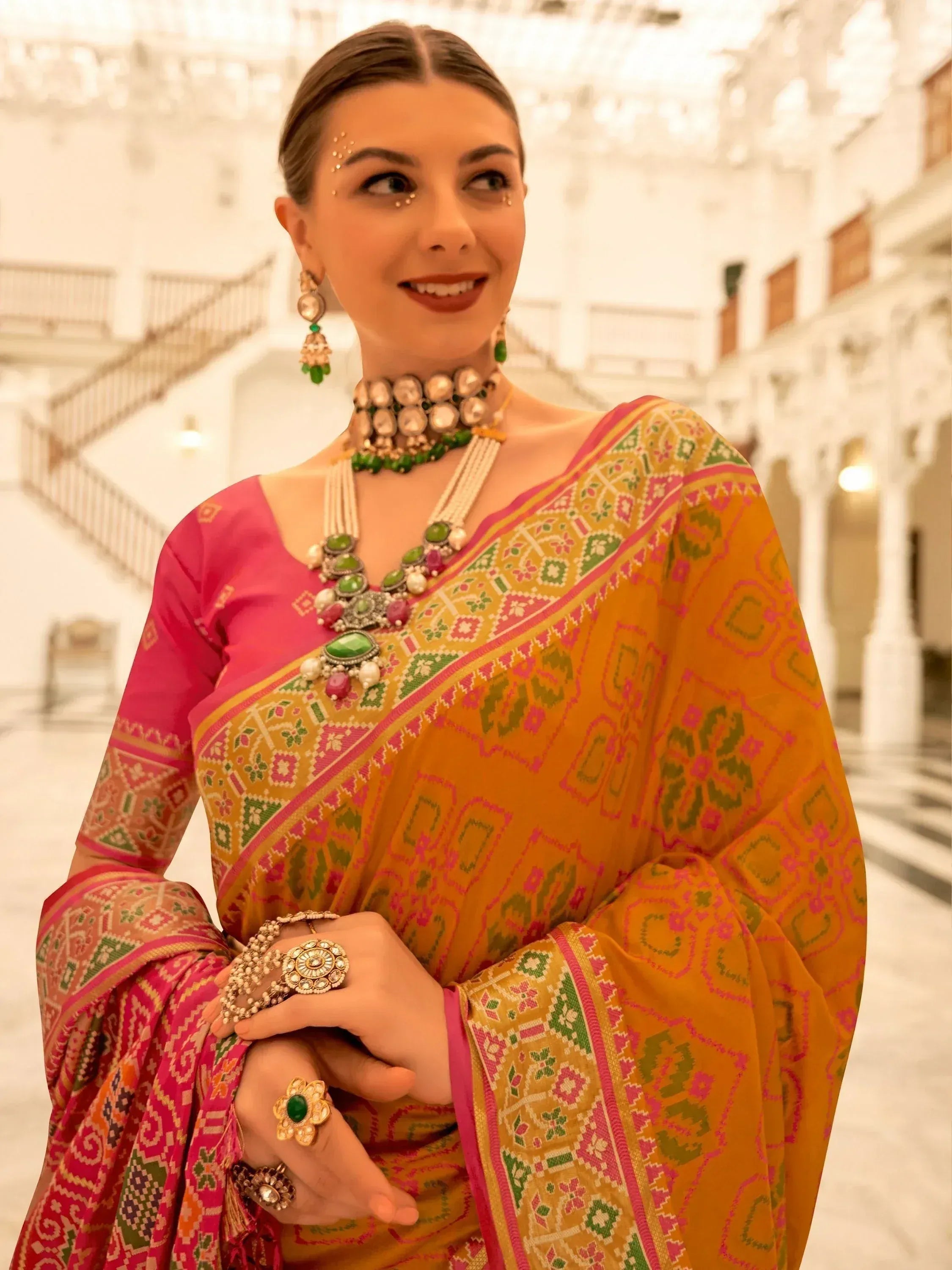 Woman in vibrant Indian saree with pink blouse, green and gold jewelry, traditional ethnic wear