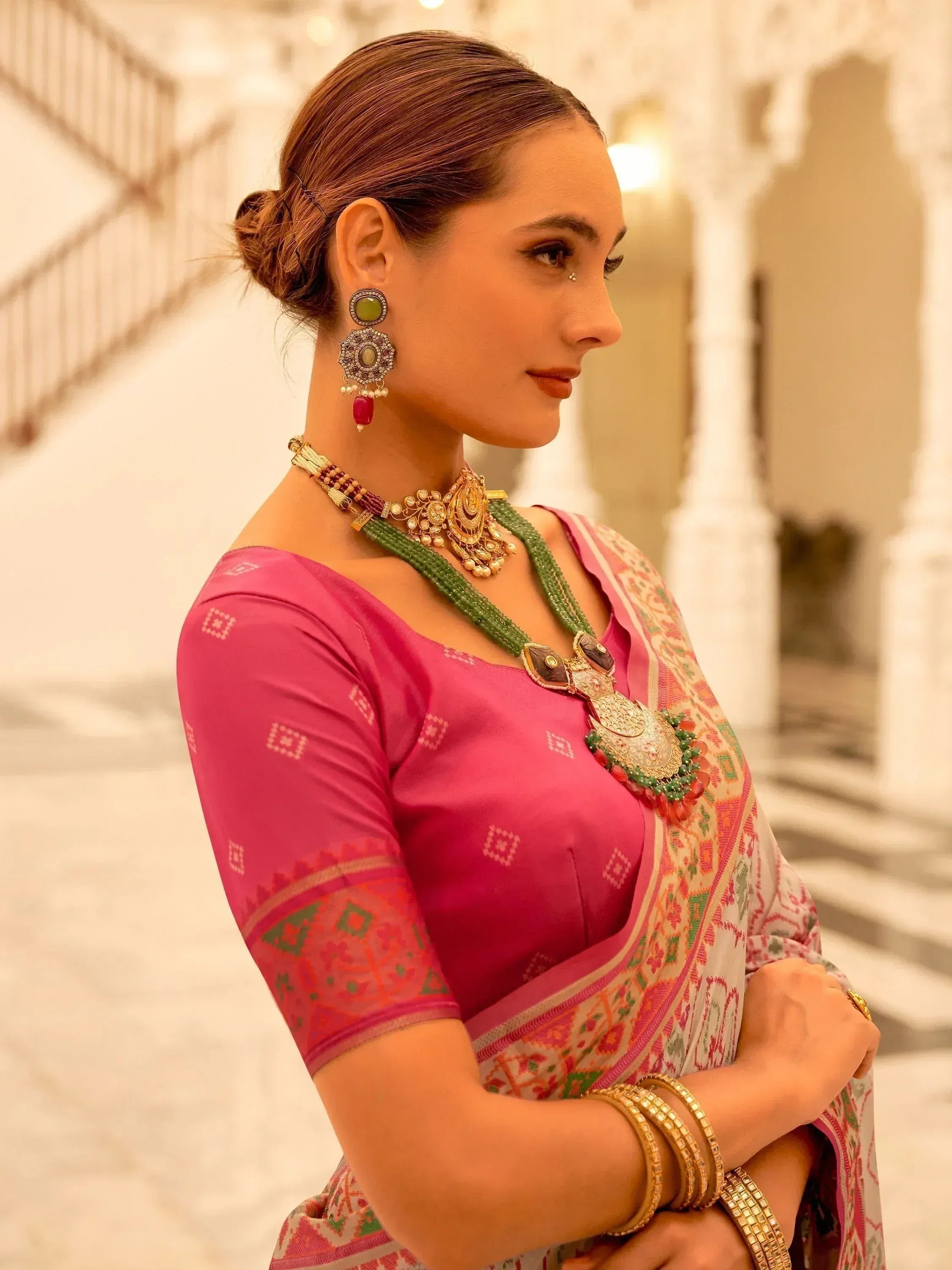 Woman in pink ethnic saree with green jewelry, traditional Indian attire for festive occasions