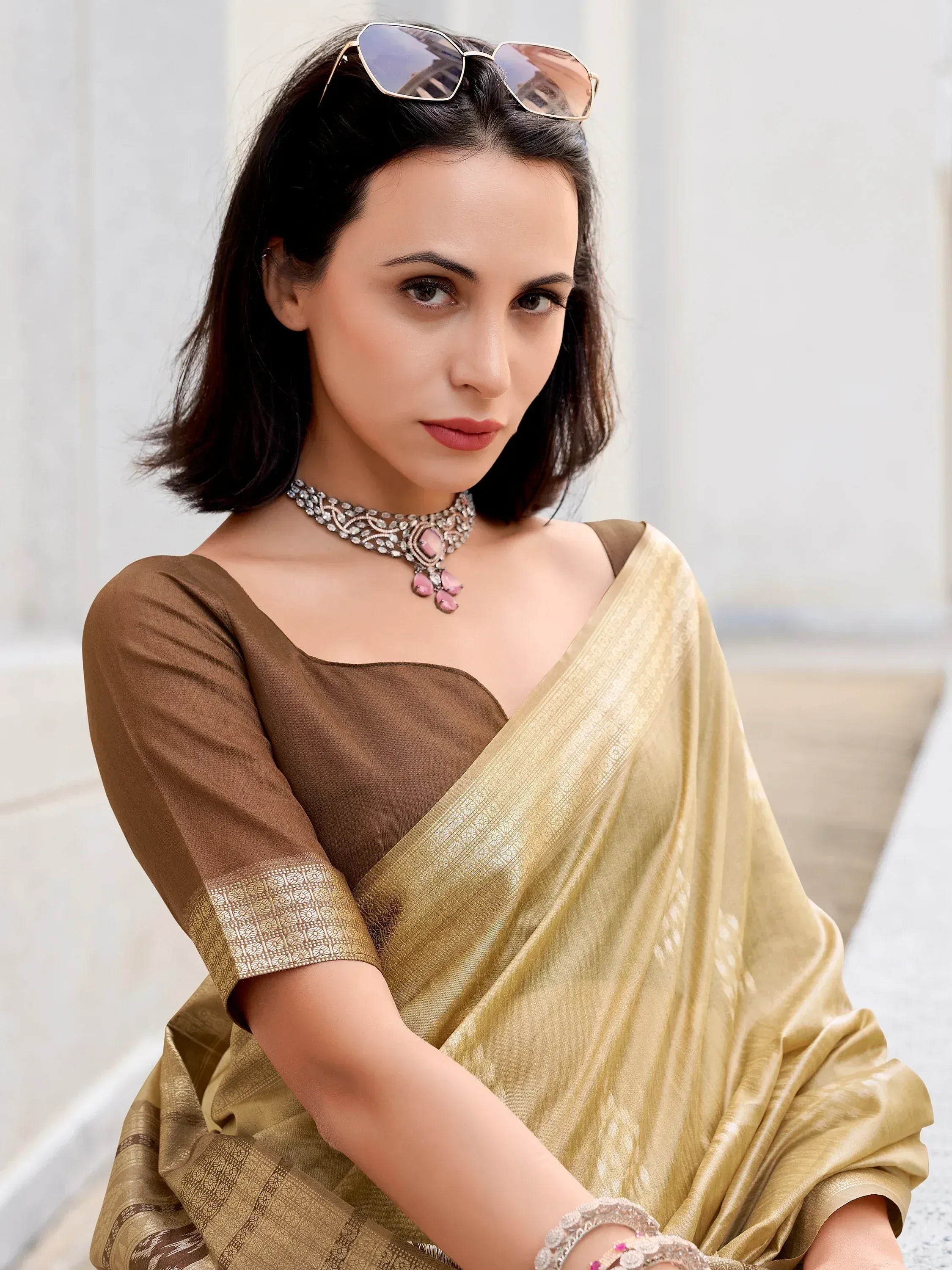 Elegant woman in golden saree with brown blouse, pink gem necklace, and sunglasses, showcasing Indian ethnic wear.