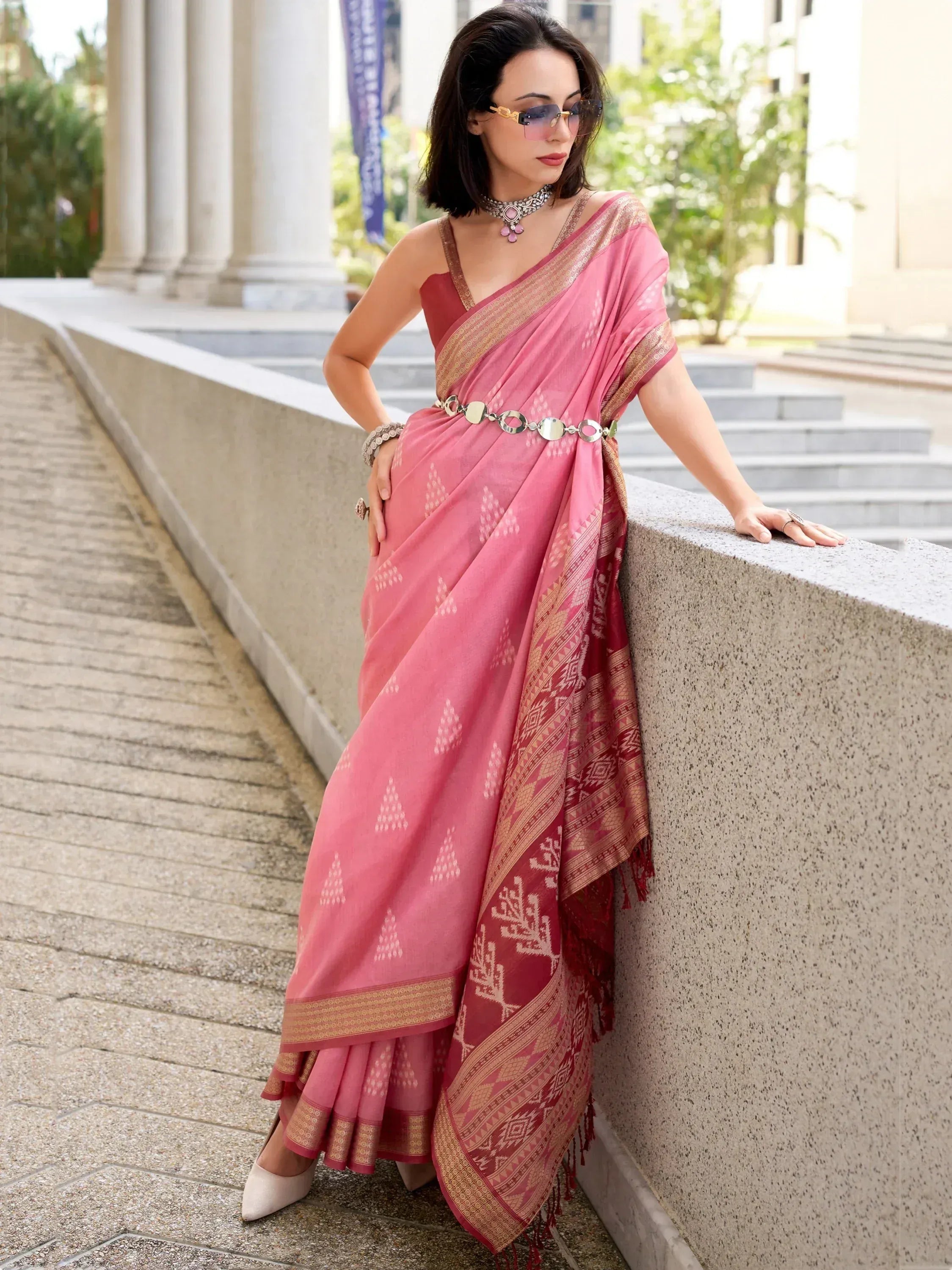 Pink designer saree with gold border and geometric print, styled with belt and choker for ethnic wear