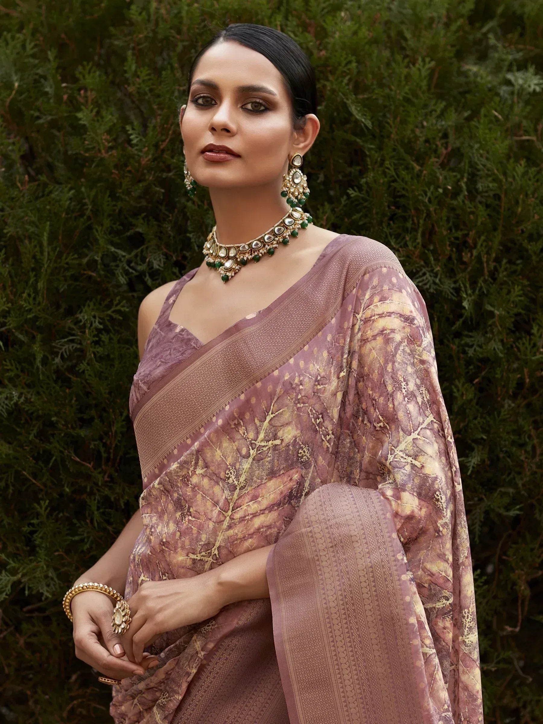 Woman in elegant mauve saree with leaf print, gold border, and traditional jewelry, styled for Indian ethnic wear.