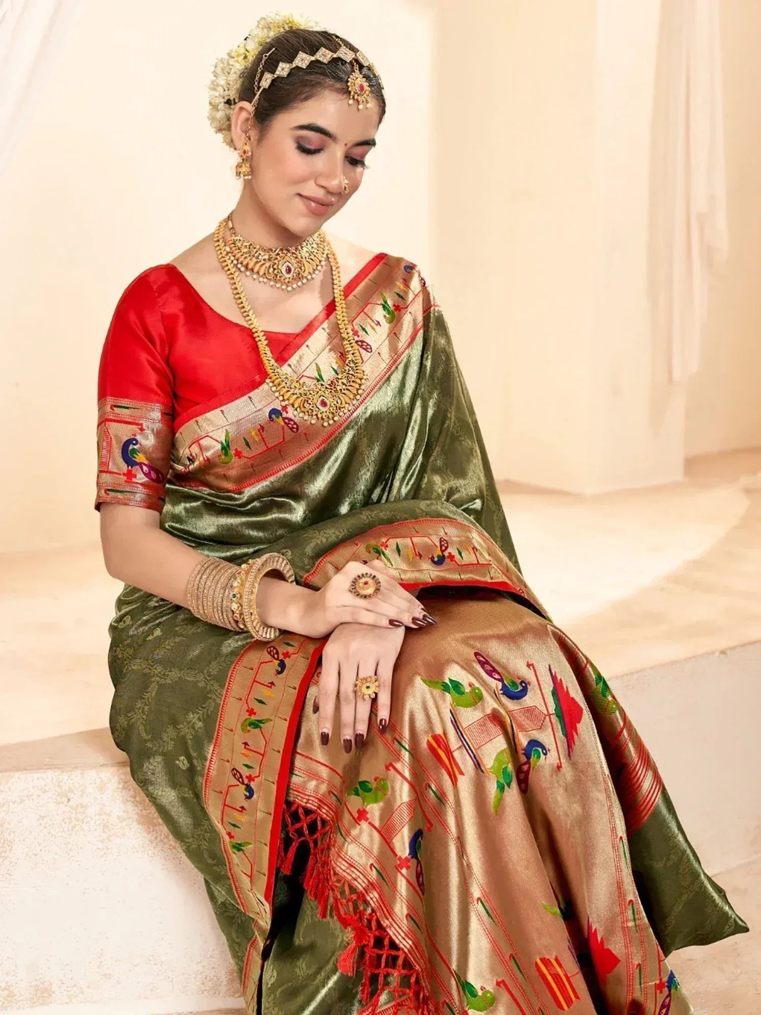 Woman in olive green and red embroidered saree with peacock motifs, traditional jewelry, and floral hair accessory