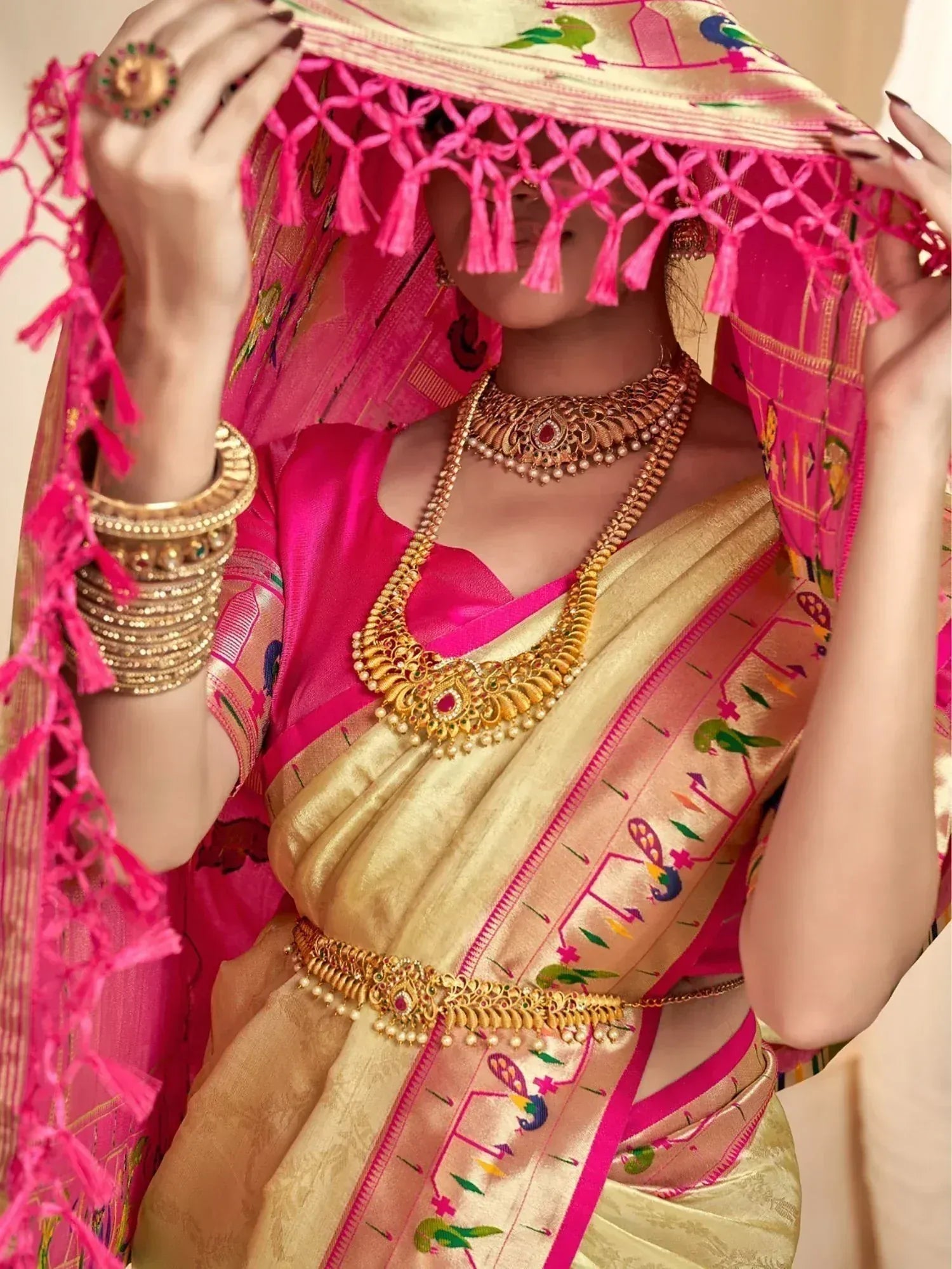 Woman in vibrant pink and gold Indian saree with peacock embroidery, tassels, and traditional gold jewelry.
