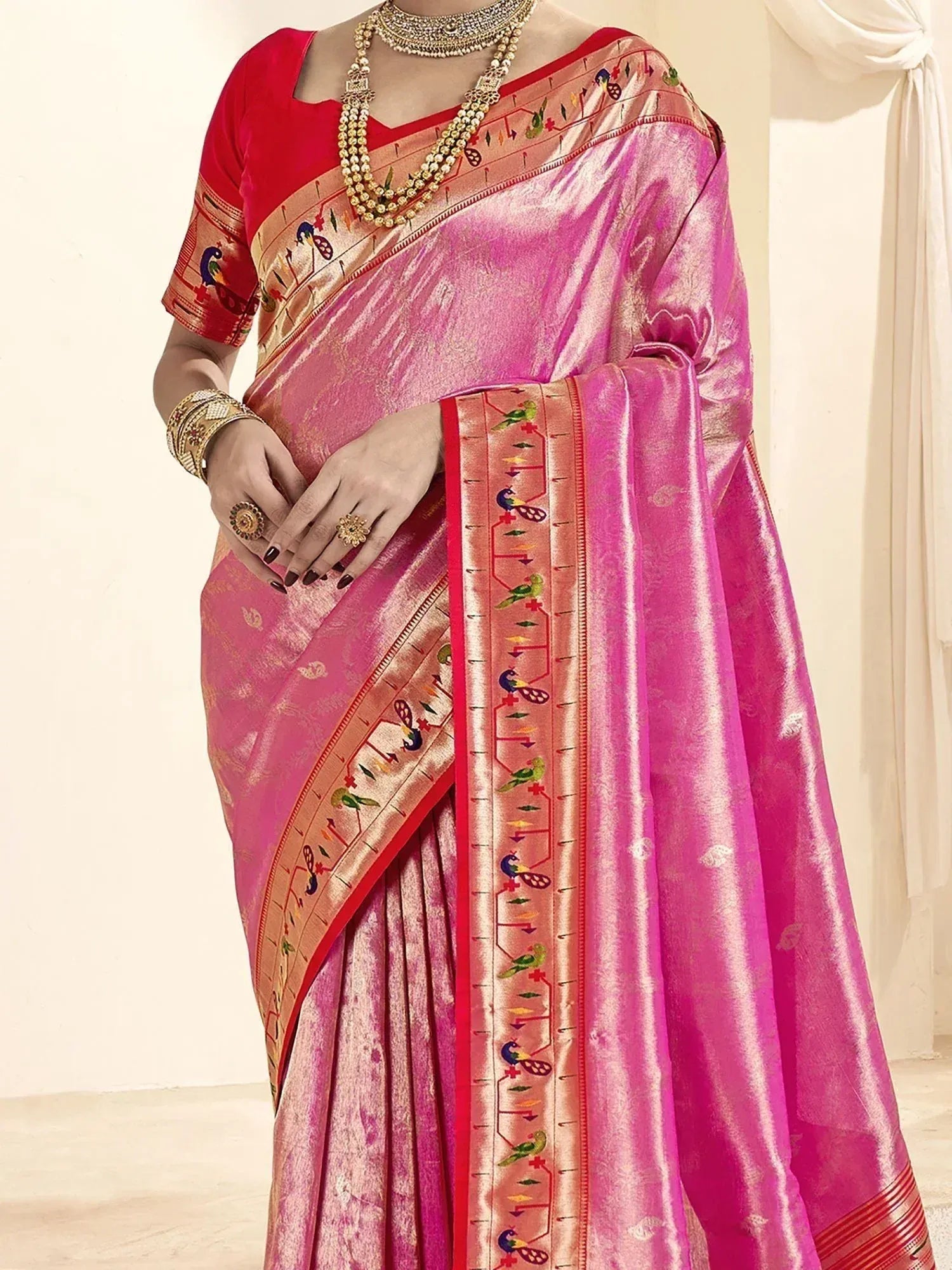 Pink silk saree with peacock border, red blouse, and gold jewelry for Indian ethnic wear