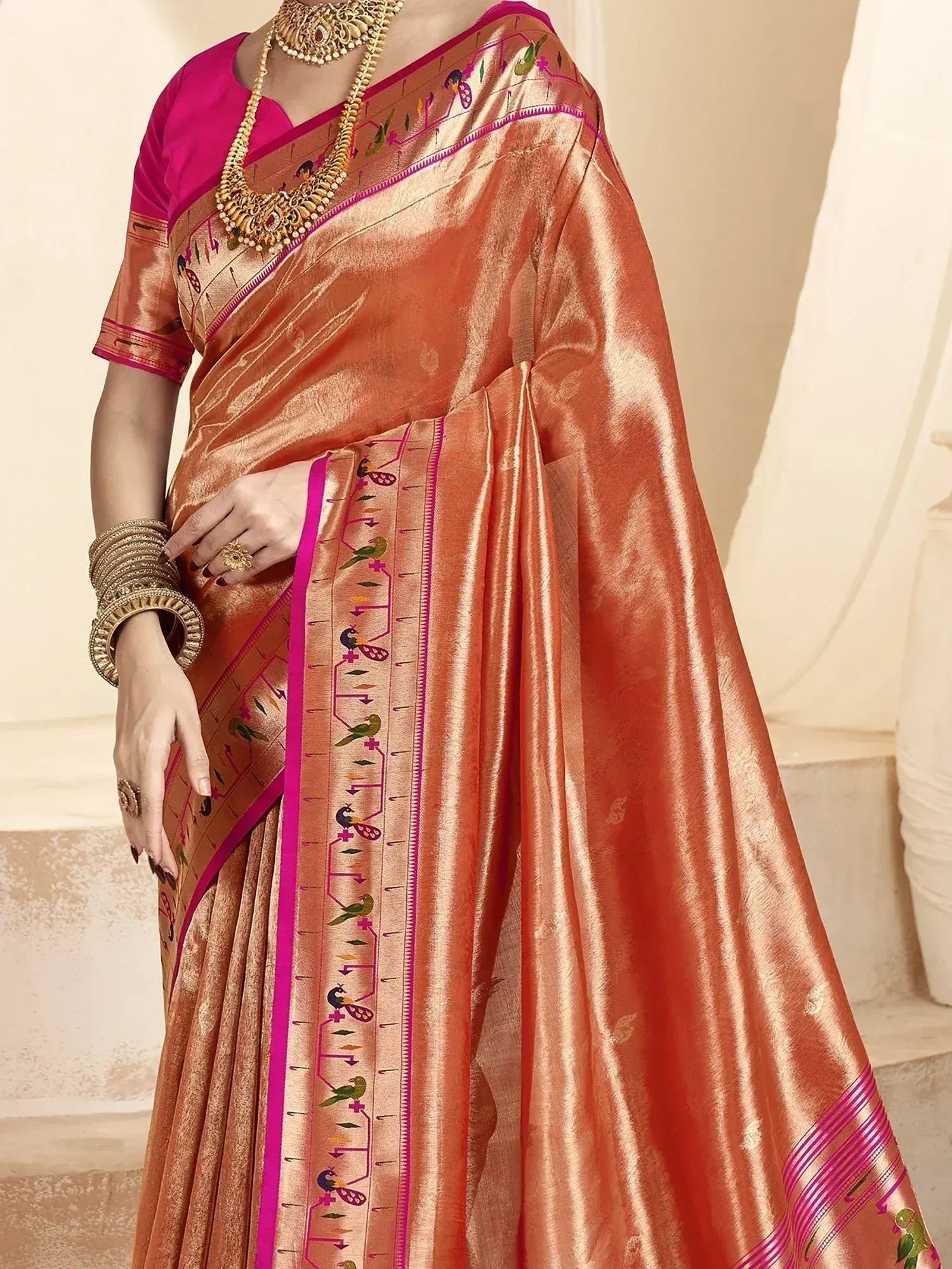 Orange silk saree with pink border and bird motifs, paired with designer blouse and gold jewelry