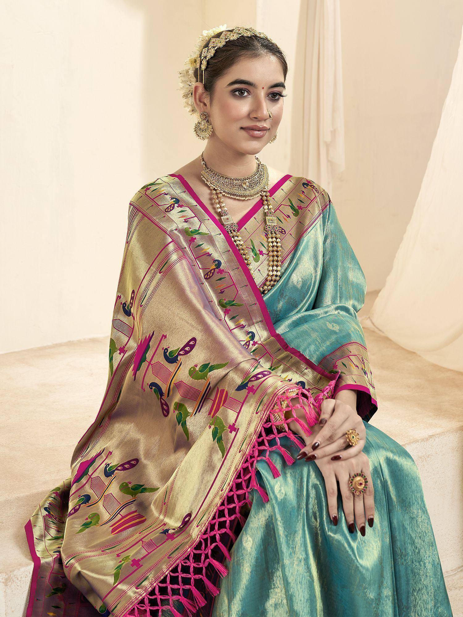 Woman in turquoise silk saree with peacock embroidery and pink border, styled with gold jewelry for ethnic occasions