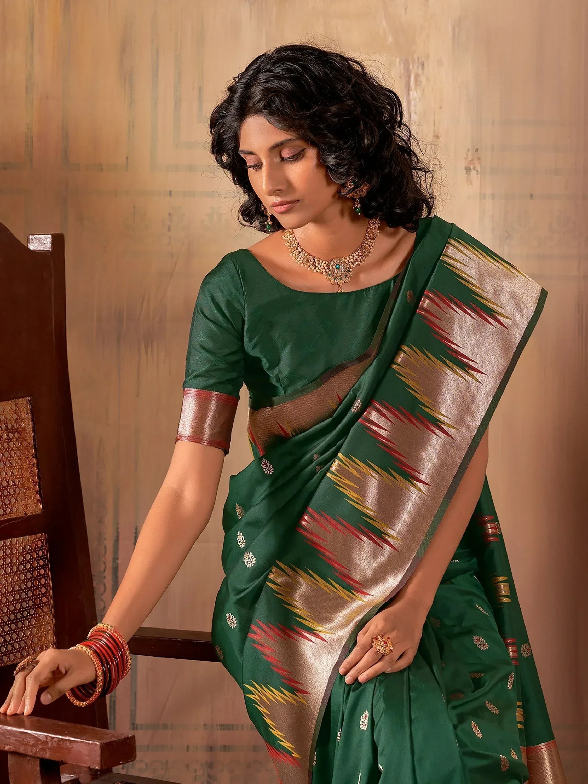Elegant green silk saree with gold and red ikat border, paired with matching blouse and traditional jewelry