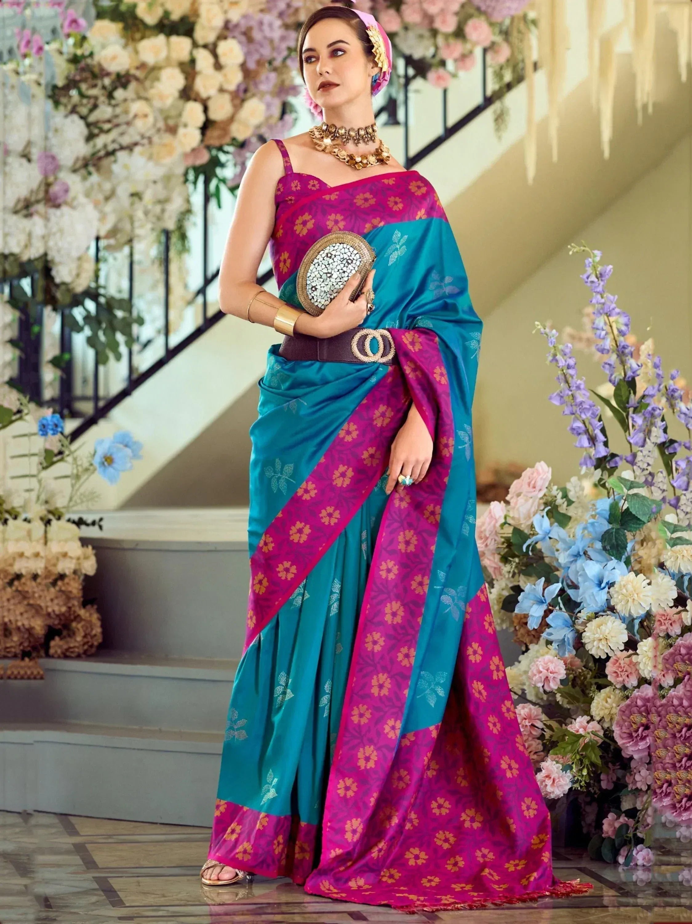 Woman in vibrant pink and teal floral saree with gold jewelry, styled for festive occasions