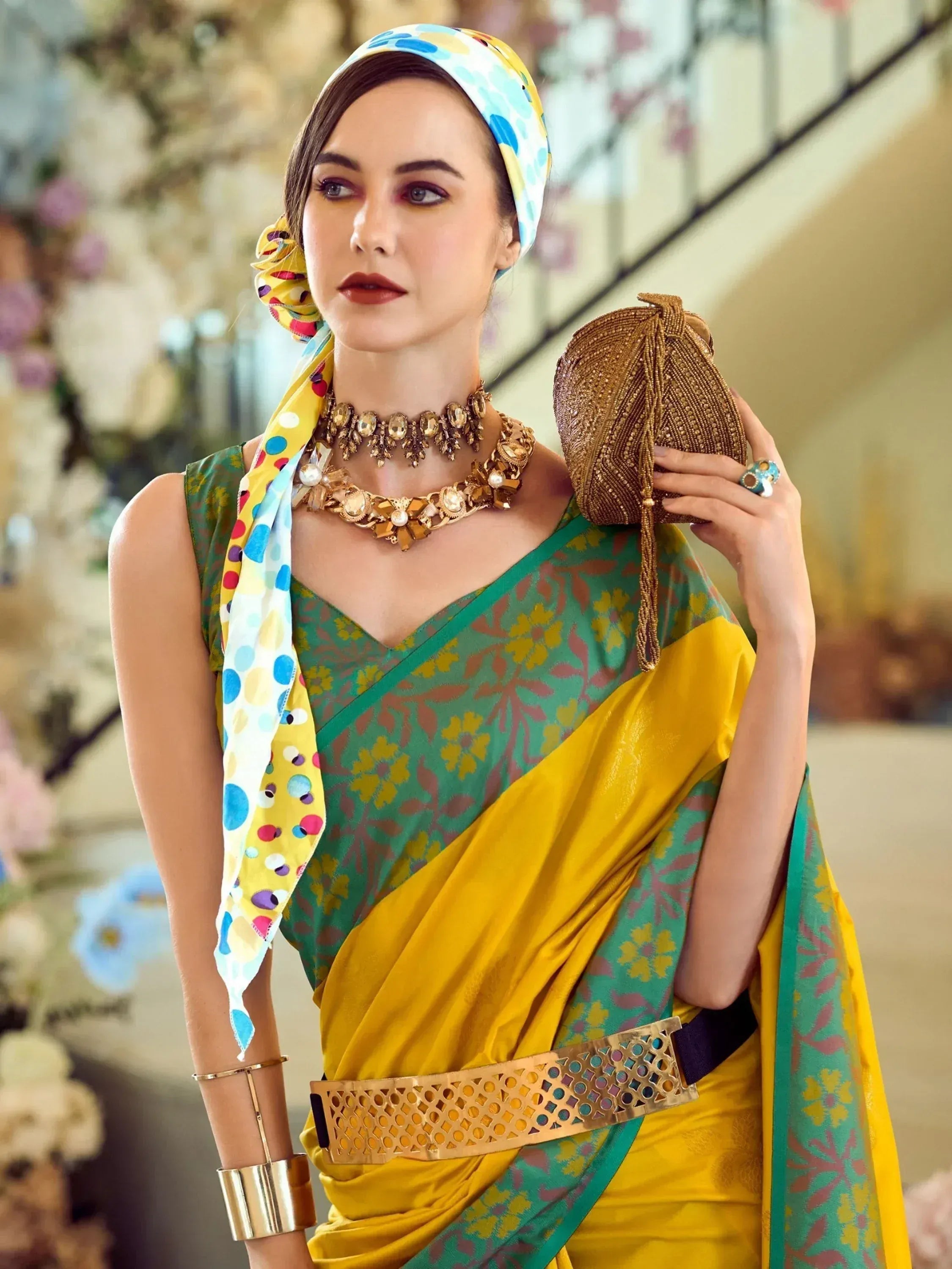 Woman in vibrant green and yellow floral saree with polka dot scarf, gold jewelry, and beaded clutch